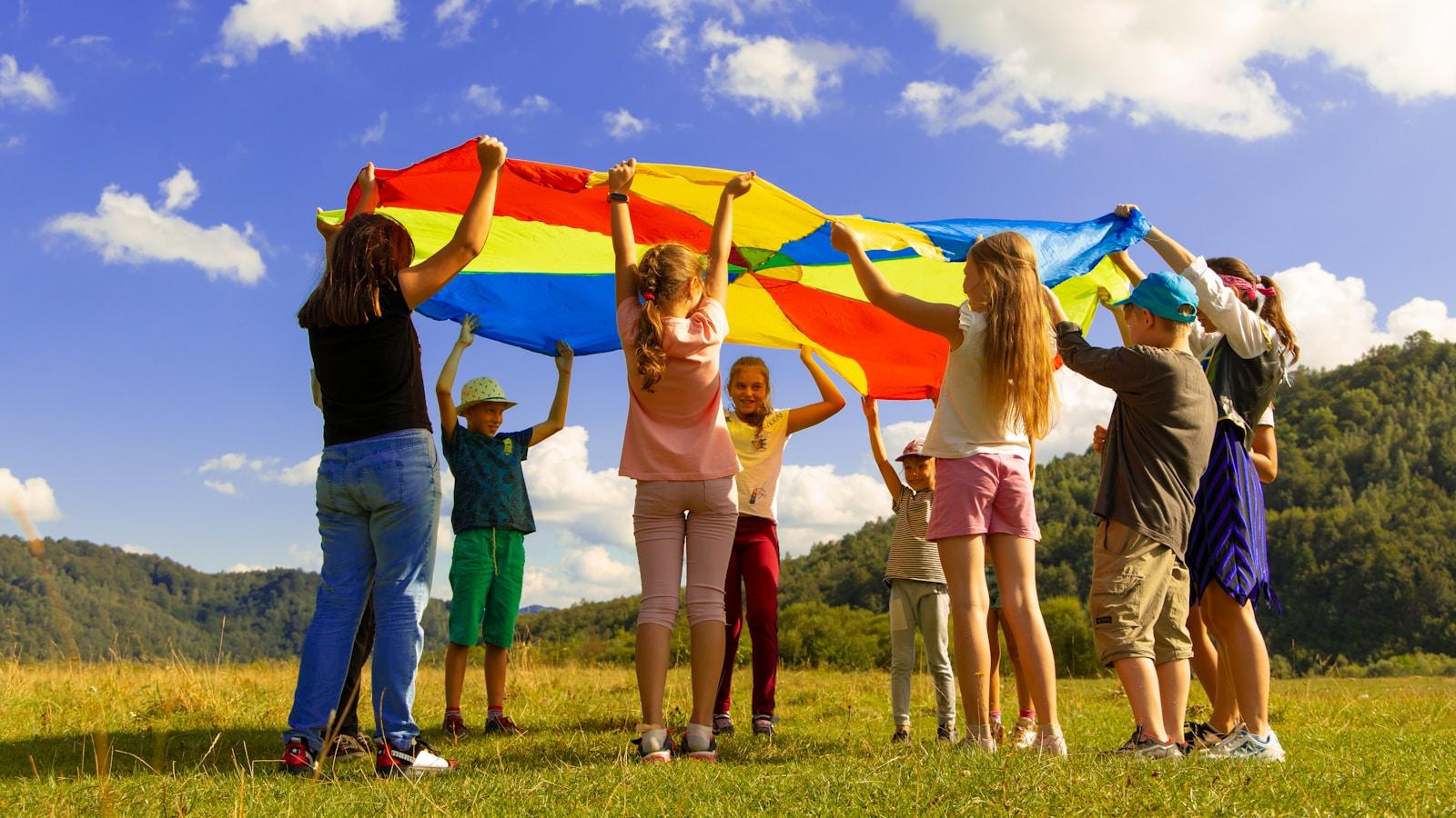 Crianças brincando ao ar livre segurando um paraquedas colorido, sob céu azul