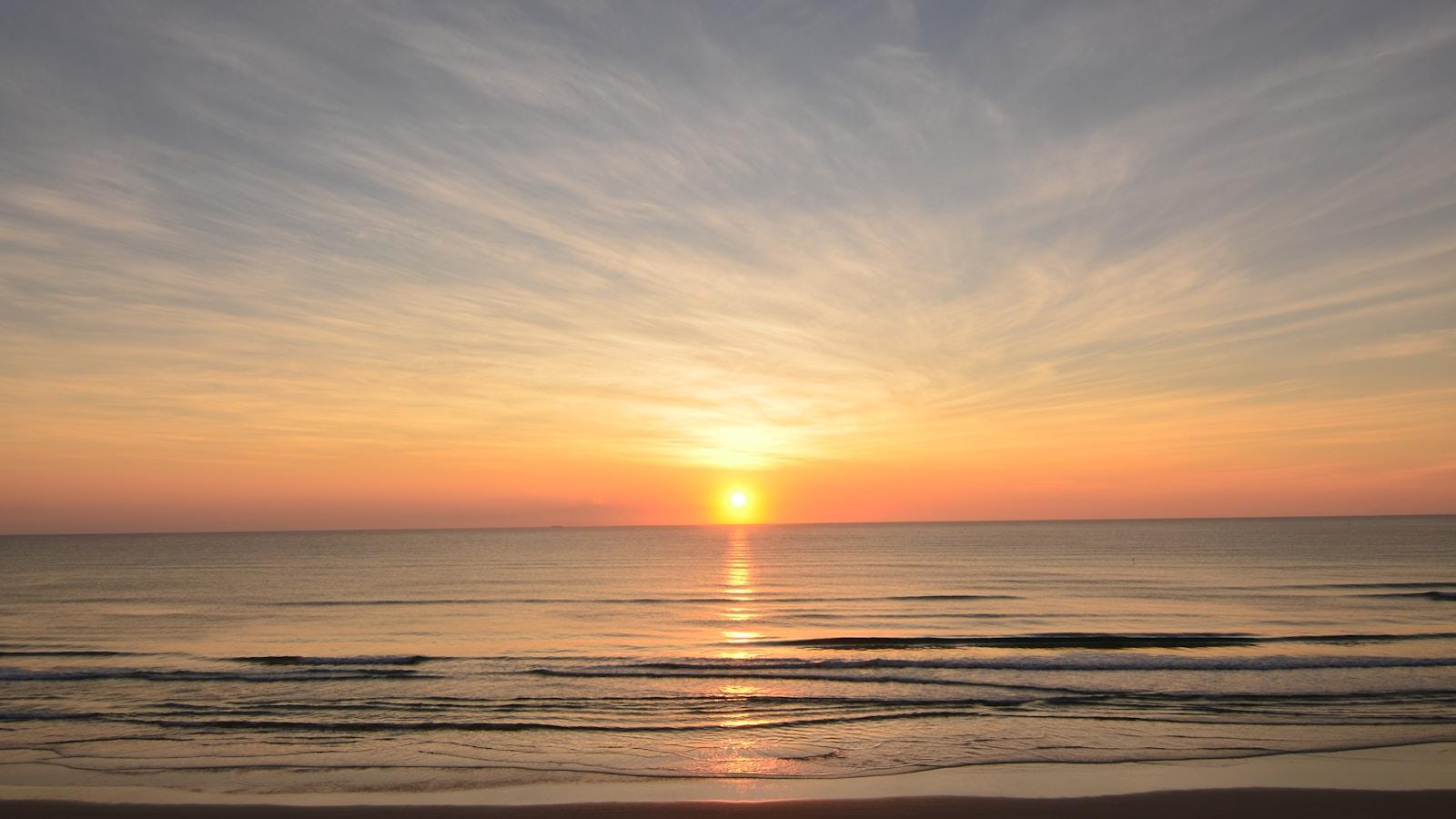 Sol nascendo sobre o mar, com o céu em tons de laranja e cinza
