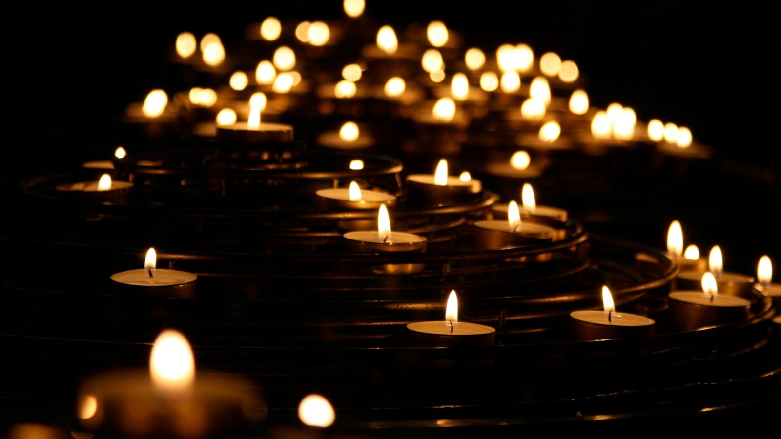 Dezenas de velas acesas em fileiras, no escuro