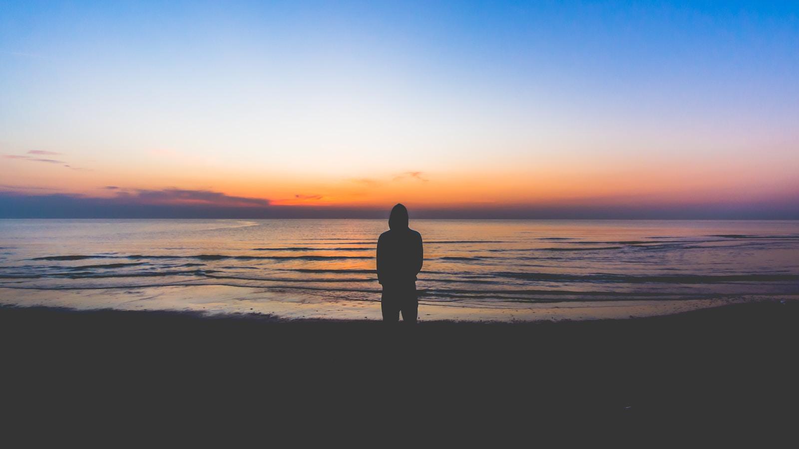 Silhueta de um homem de pé diante do mar, ao amanhecer