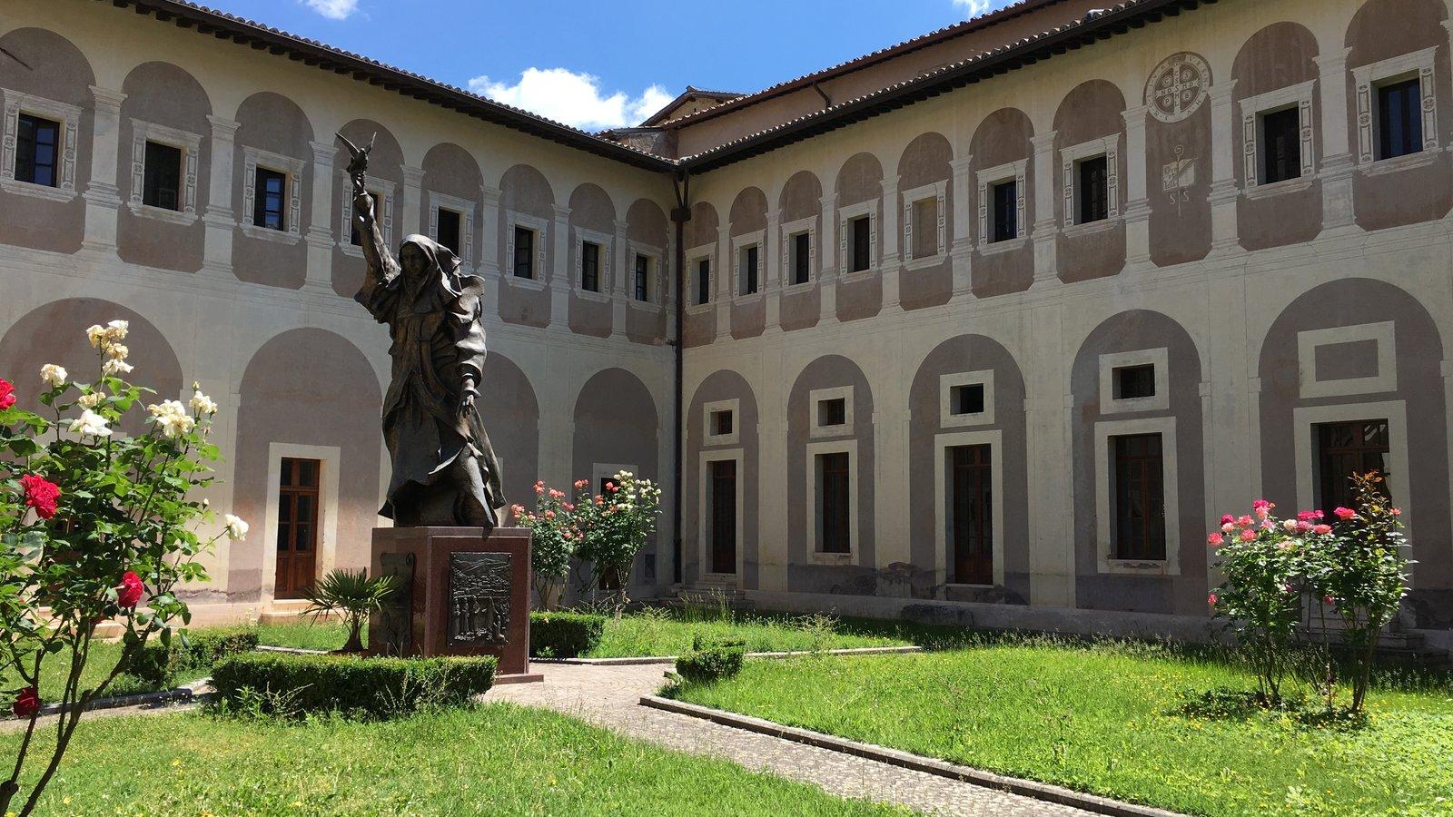 Claustro de um mosteiro, com estátua de santo e jardim de roseiras