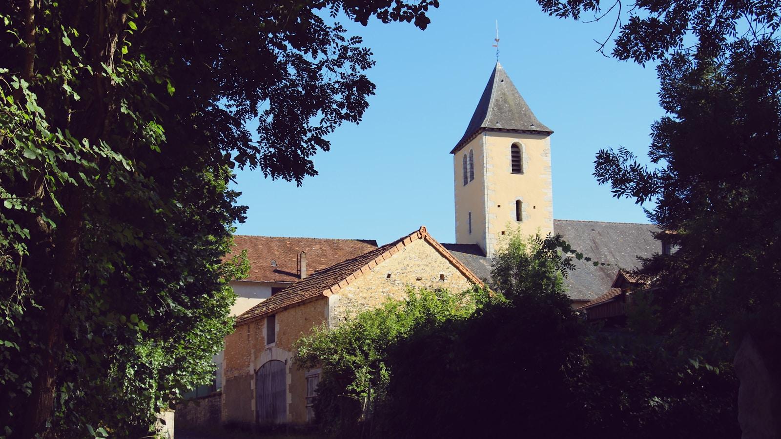 Torre de igreja de pedra com telhado de ardósia numa vila francesa, entre árvores