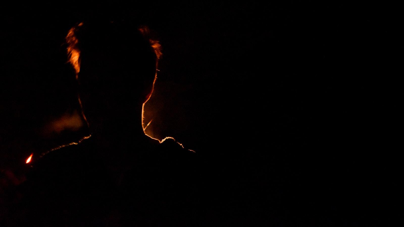Silhueta de uma pessoa contornada por uma luz de fogo, na escuridão