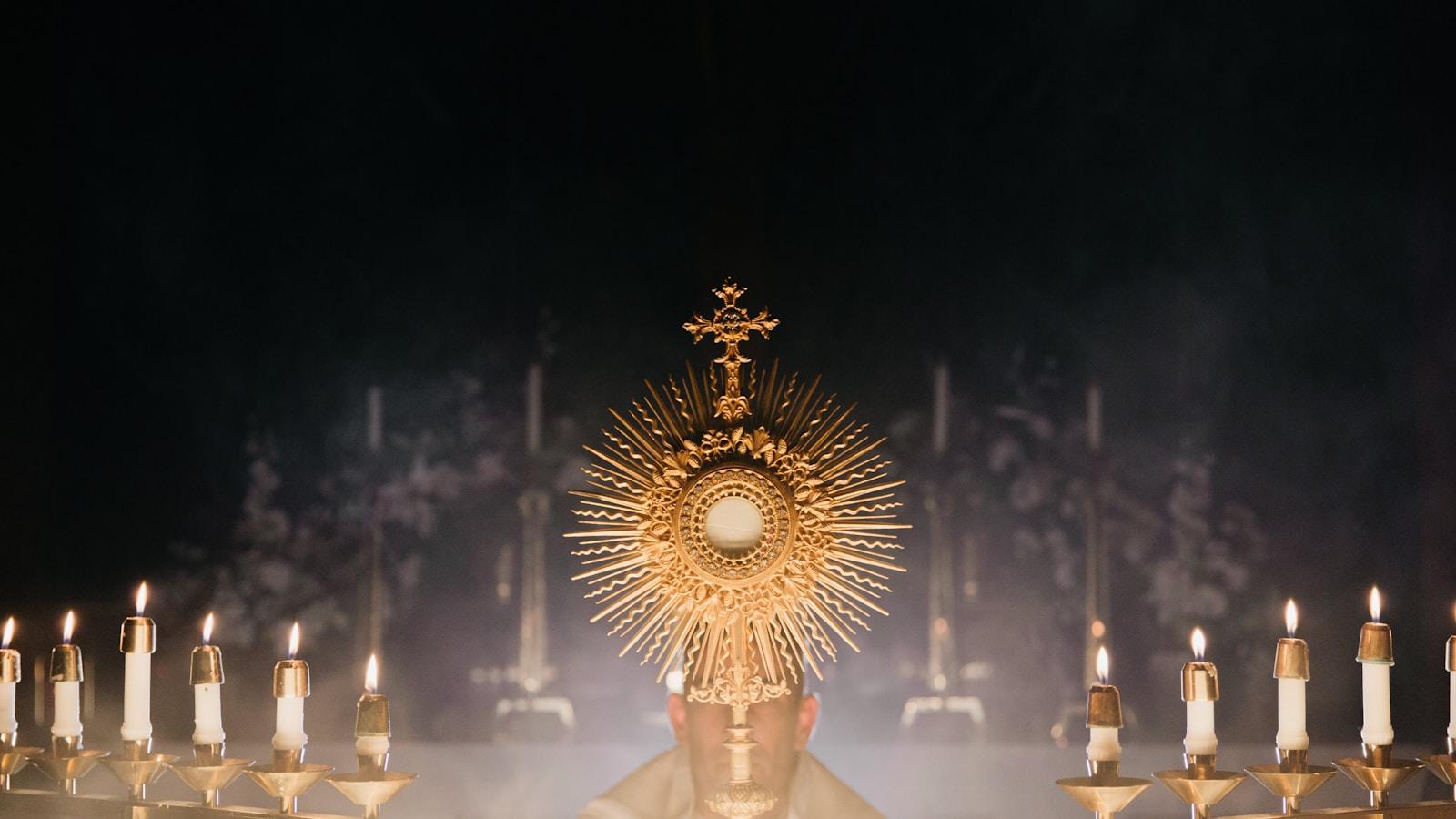 Ostensório dourado sobre o altar entre velas acesas, envolto em fumaça de incenso