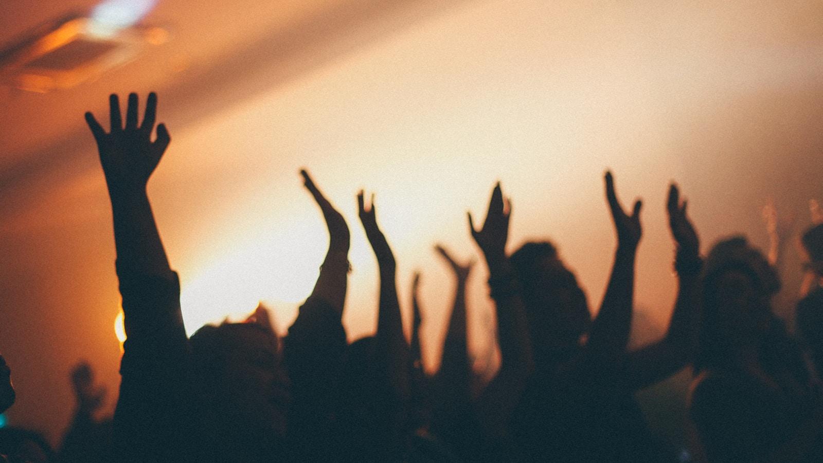 Silhuetas de pessoas com as mãos erguidas, contra uma luz alaranjada