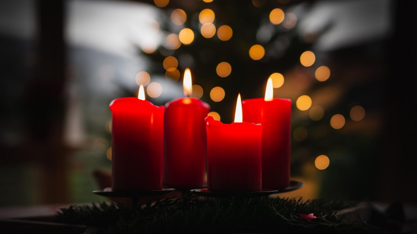 Quatro velas vermelhas acesas numa coroa do Advento, com luzes de Natal ao fundo