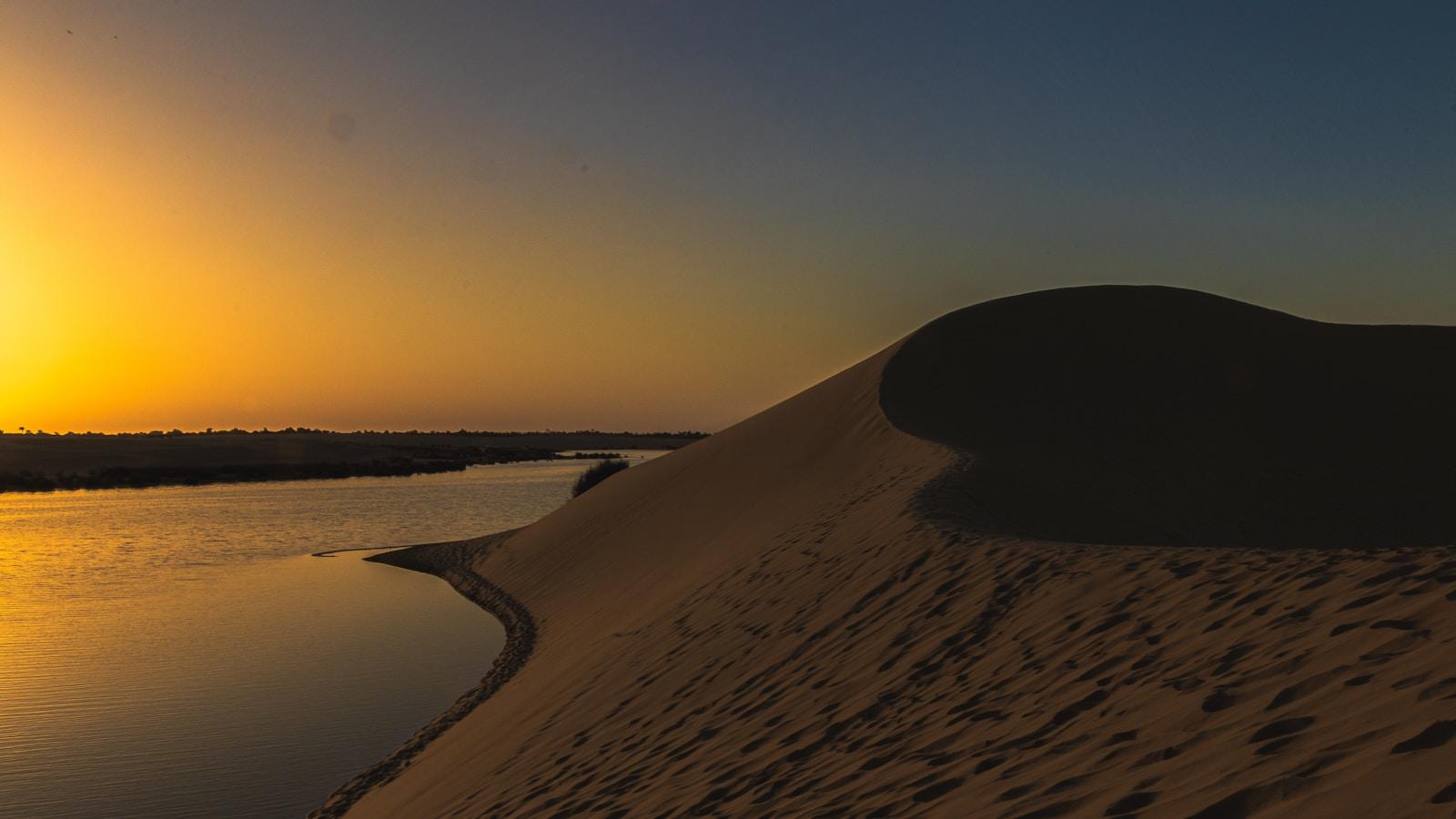 Duna de areia à beira de um lago no deserto, ao pôr do sol