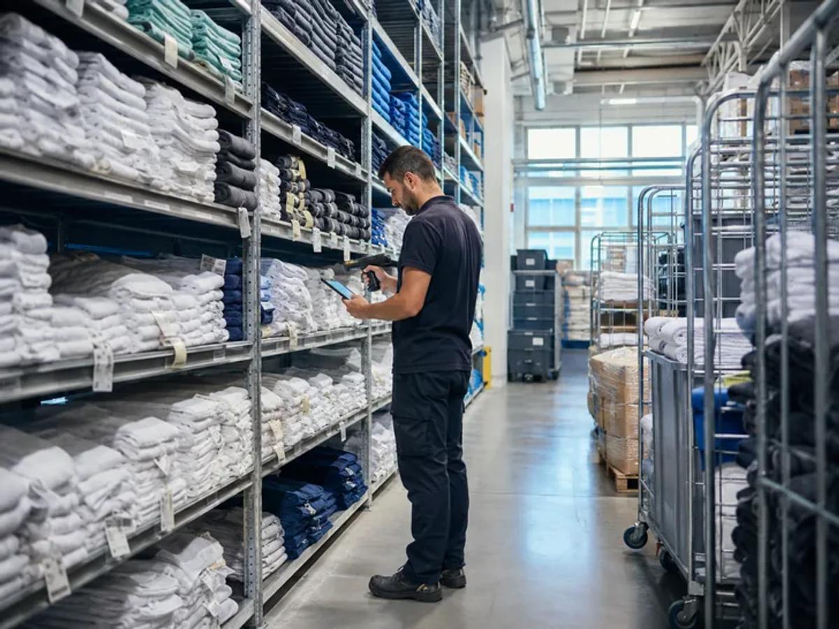 A worker between tall shelves stacked with folded white linen