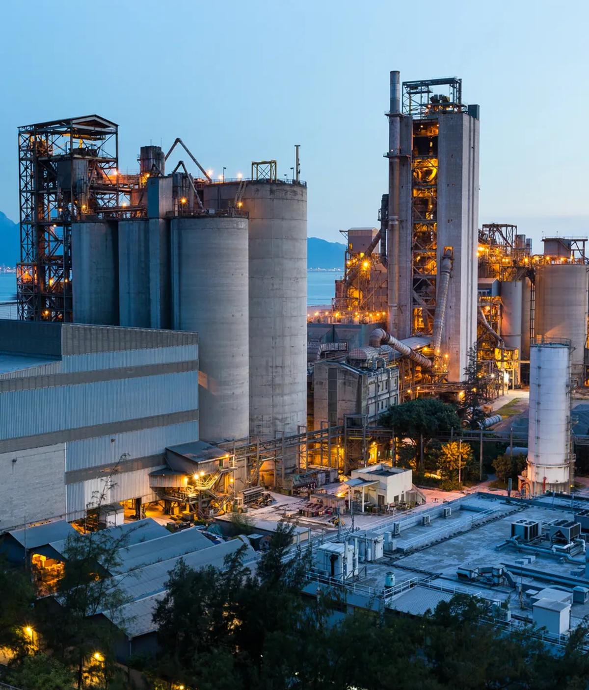 An industrial plant lit at dusk, silos and pipework rising above a service yard
