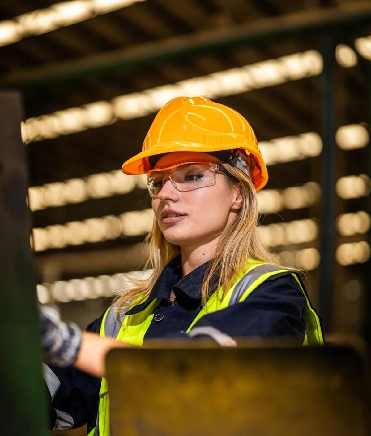 A worker in a hard hat and hi-vis jacket operating a machine in an industrial hall