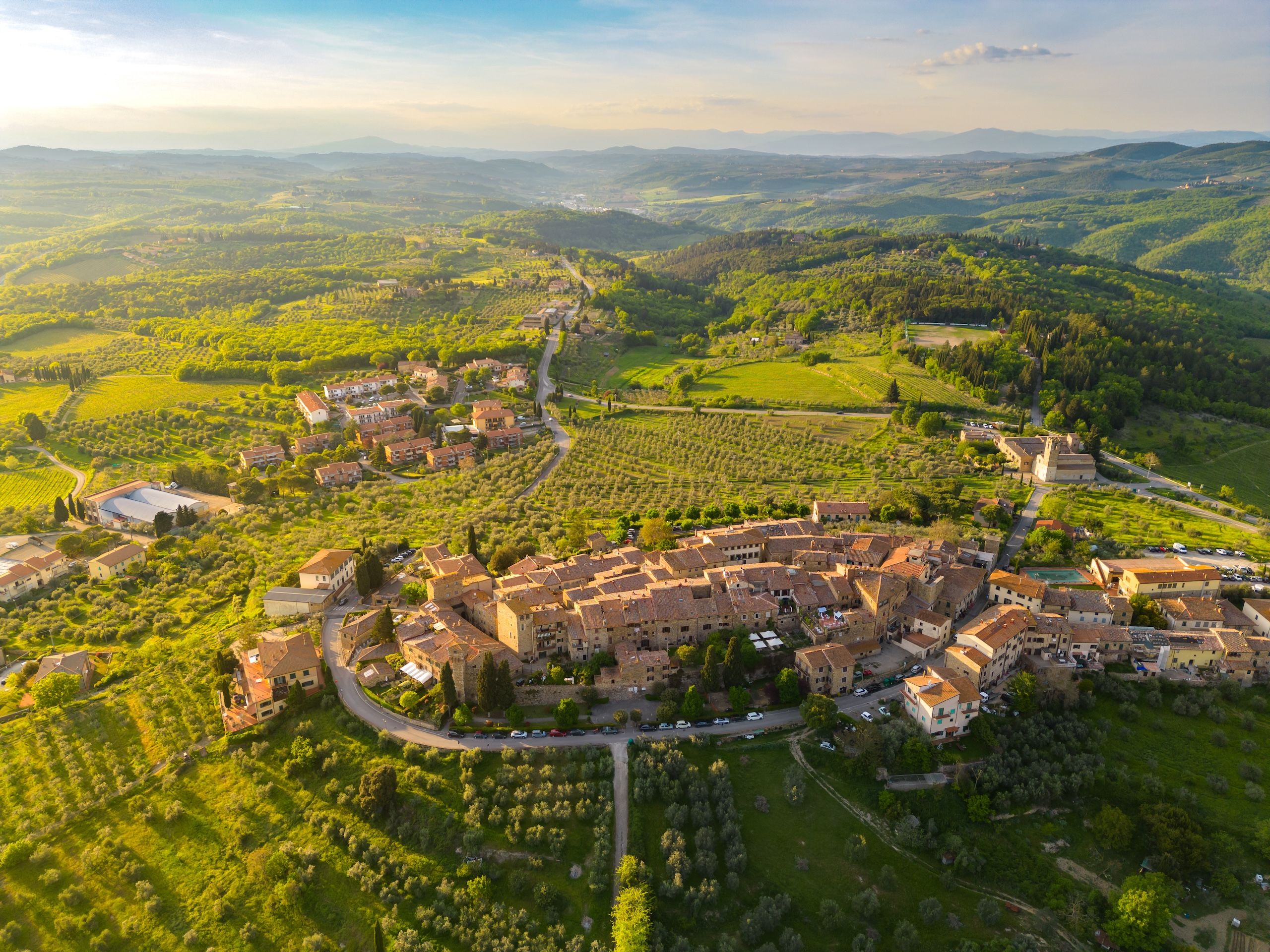 En sjarmerende landsby i Toscana, sett ovenfra, omgitt av grønne åkrer og olivenlunder.