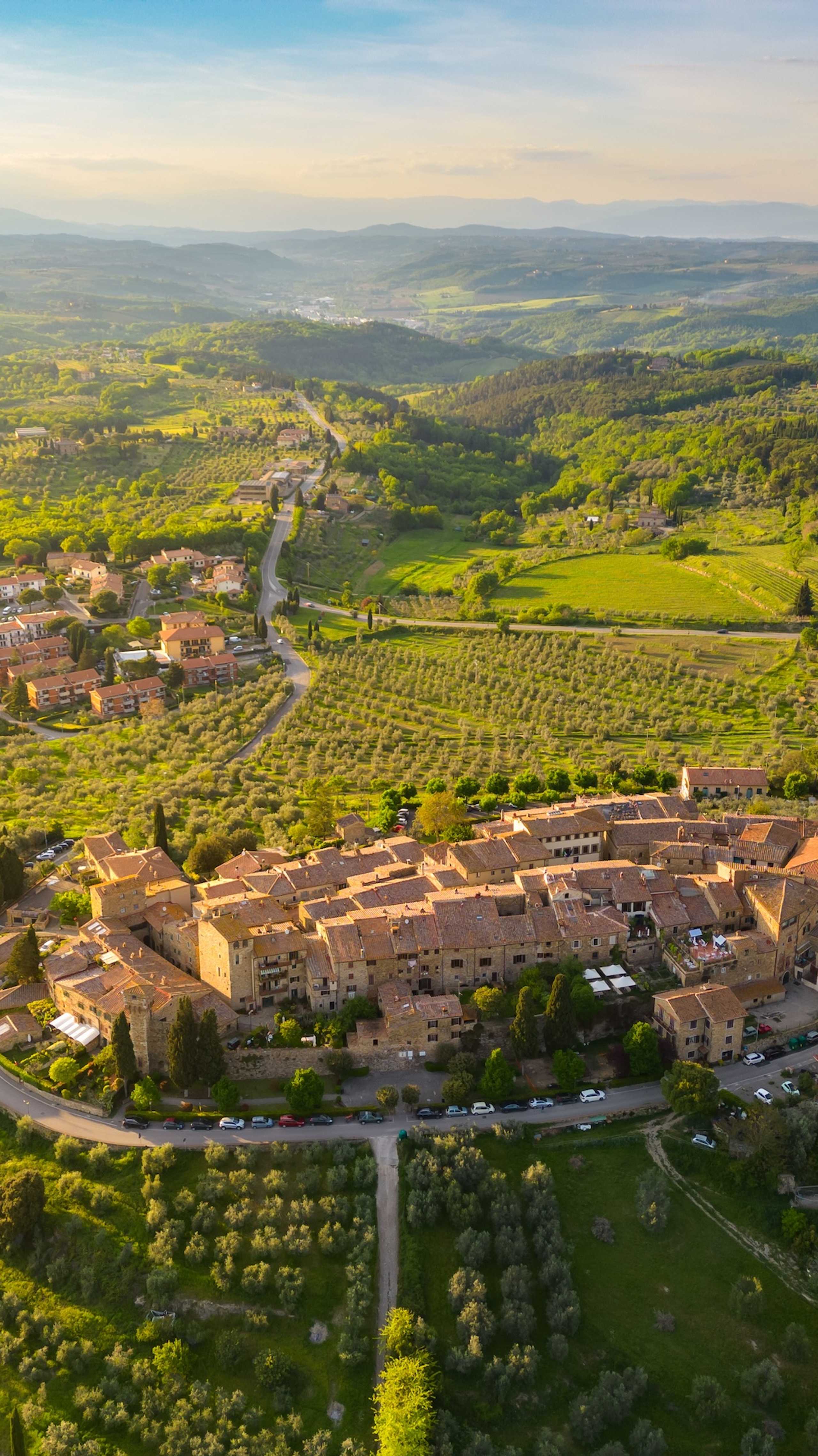 En sjarmerende landsby i Toscana, sett ovenfra, omgitt av grønne åkrer og olivenlunder.