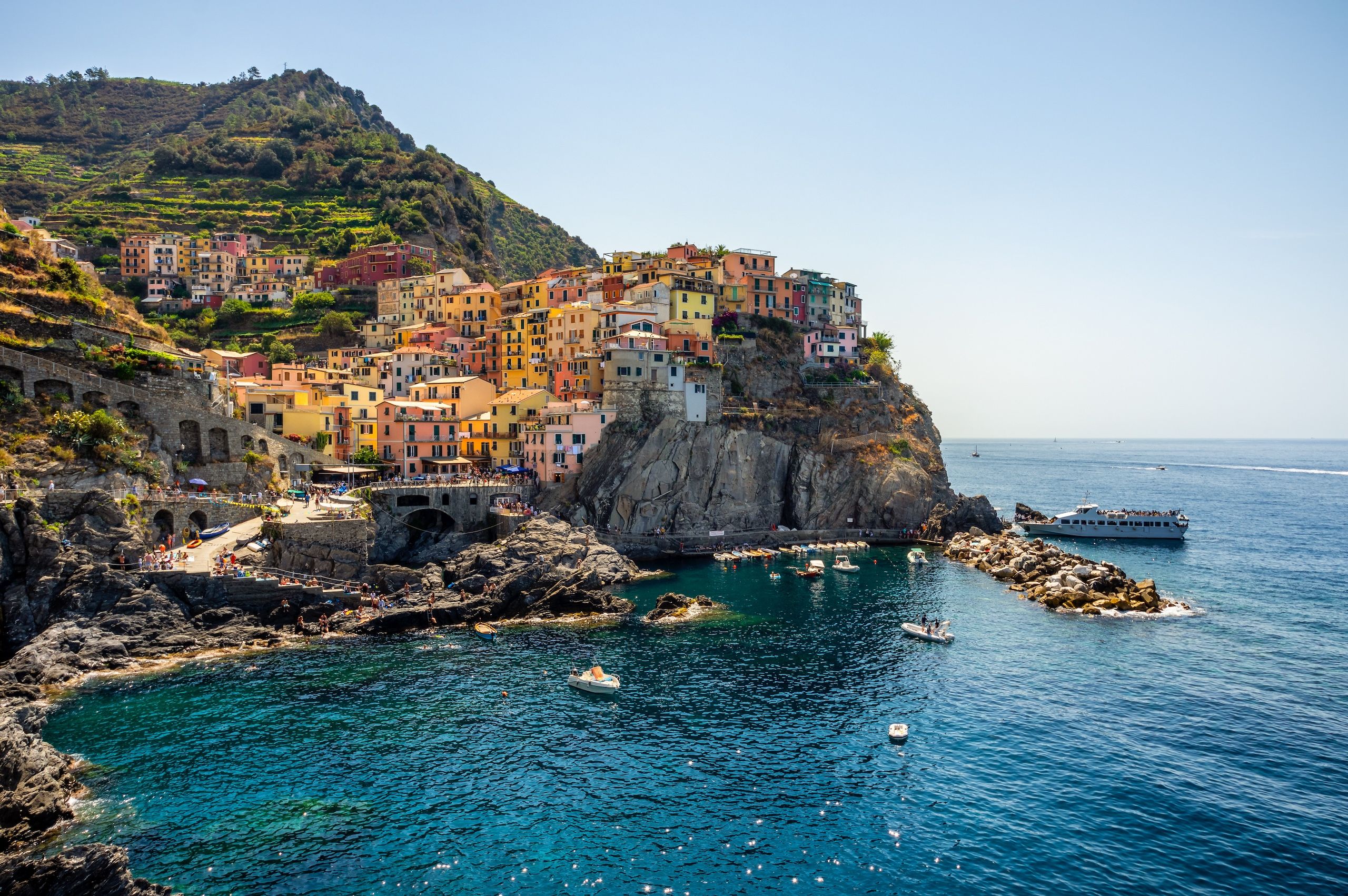 Fargerike bygninger som ligger på klipper ved kysten av Cinque Terre, Italia, omgitt av blått hav og terrasserte åser.