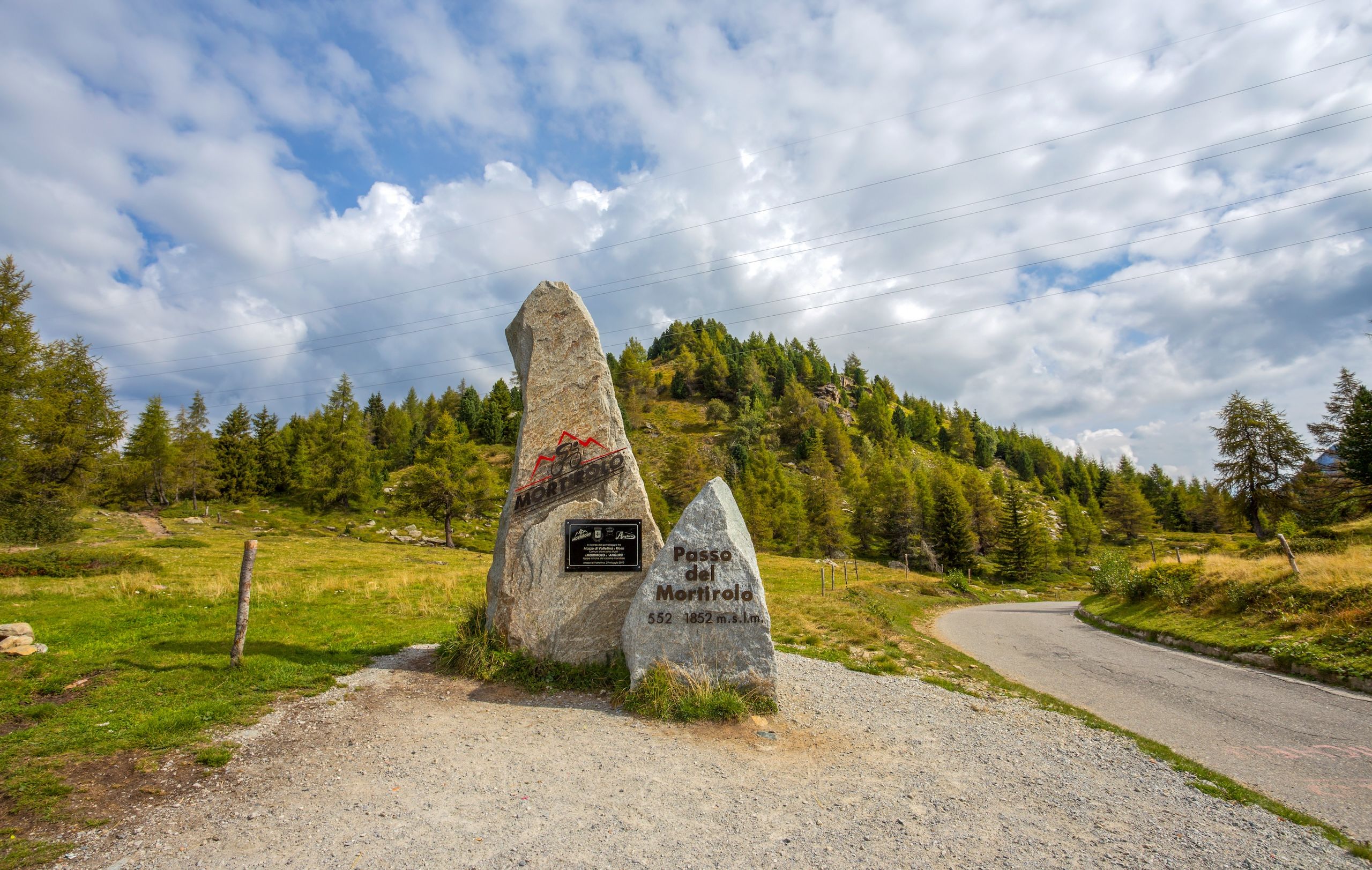 Passo del Mortirolo i de italienske Alpene med en veiskiltstein og frodig grønt landskap rundt.