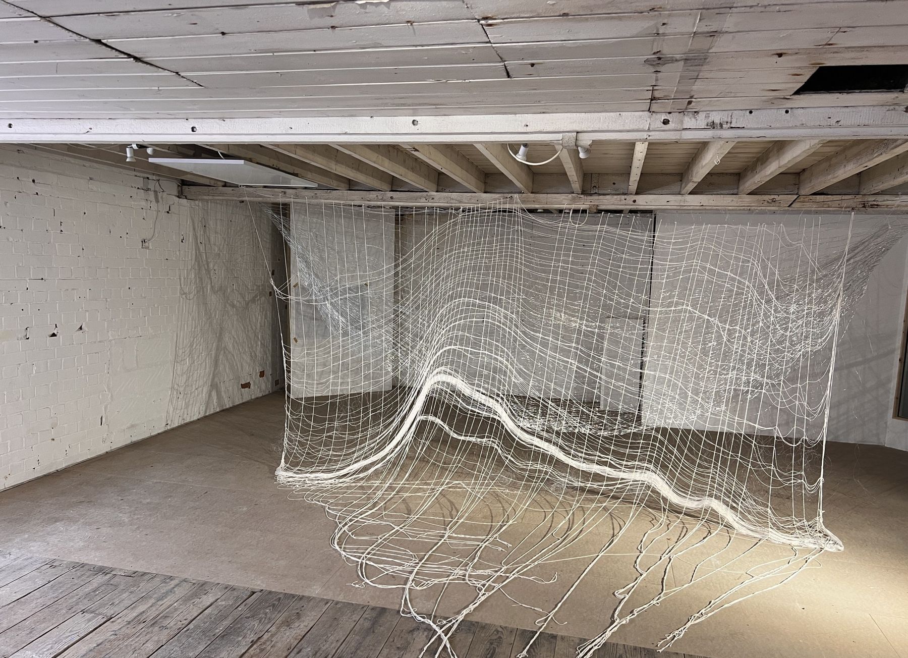 Layers of woven nets suspended in a light-filled room at the Old Tannery, cascading towards the wooden floor.