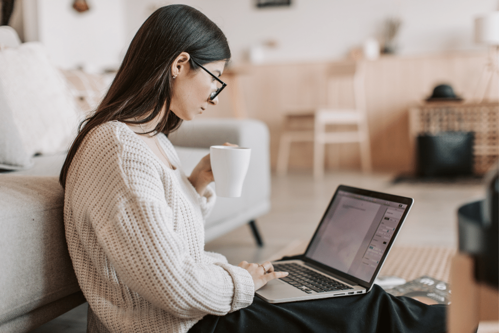 A woman is sitting on the floor as she browses the internet on her laptop
