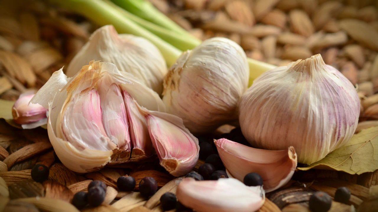 Whole garlic bulbs and separated cloves showing their pink-purple skins on a wooden board