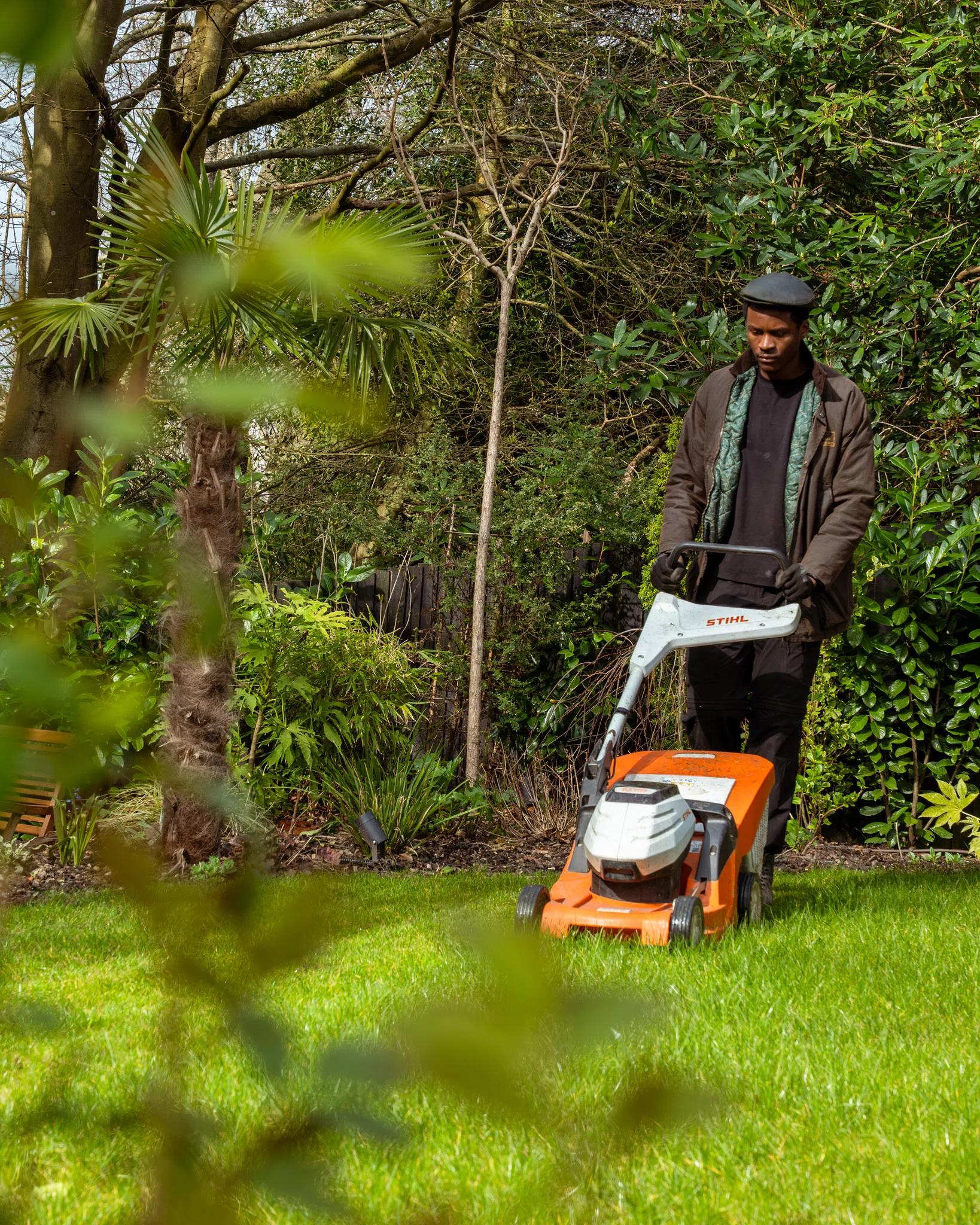 A Willow Alexander gardener mowing an overgrown lawn during a garden clearance.