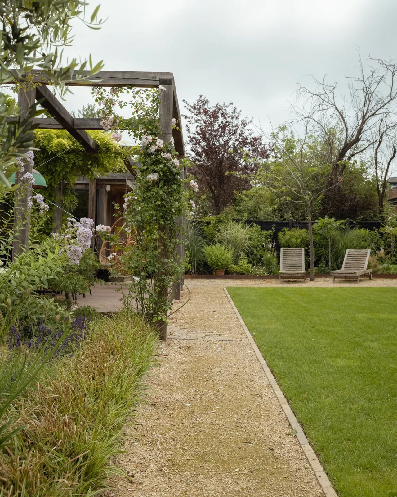 An oak pergola dressed in climbing roses beside a gravel path