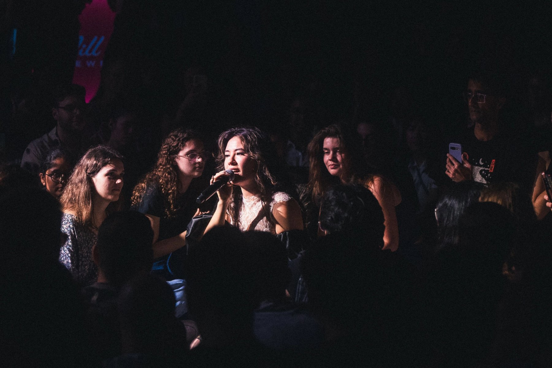 Emei sits among the crowd on the floor, singing "Dear Emily"