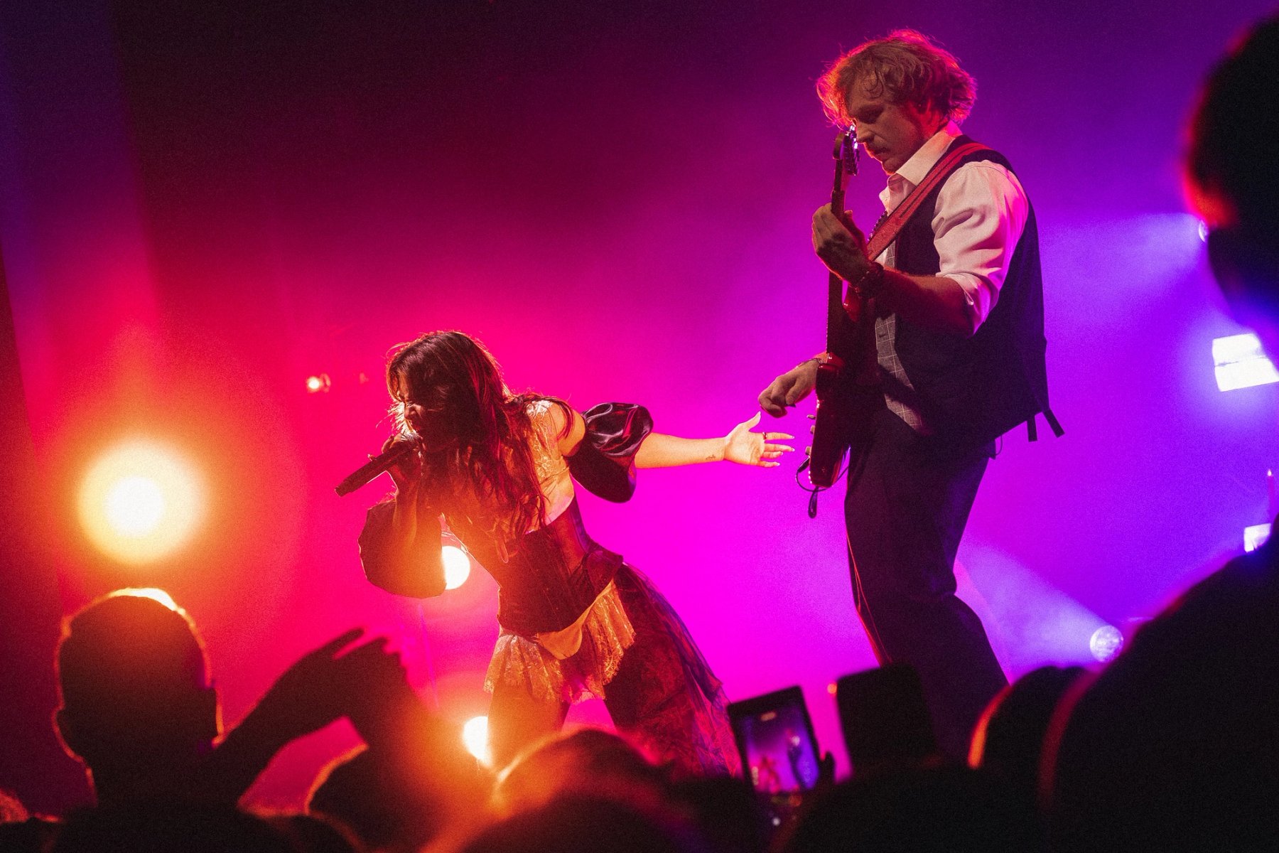Emei reaches towards her guitarist in pink and orange light at the Danforth Music Hall