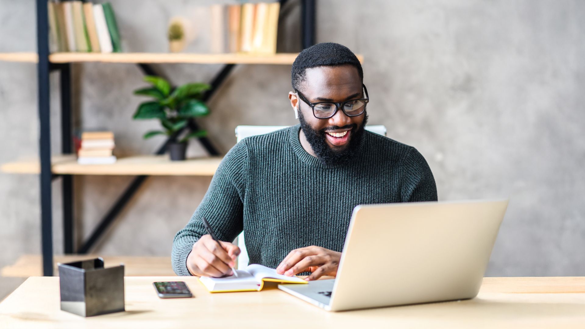 Smiling man taking notes while at a computer