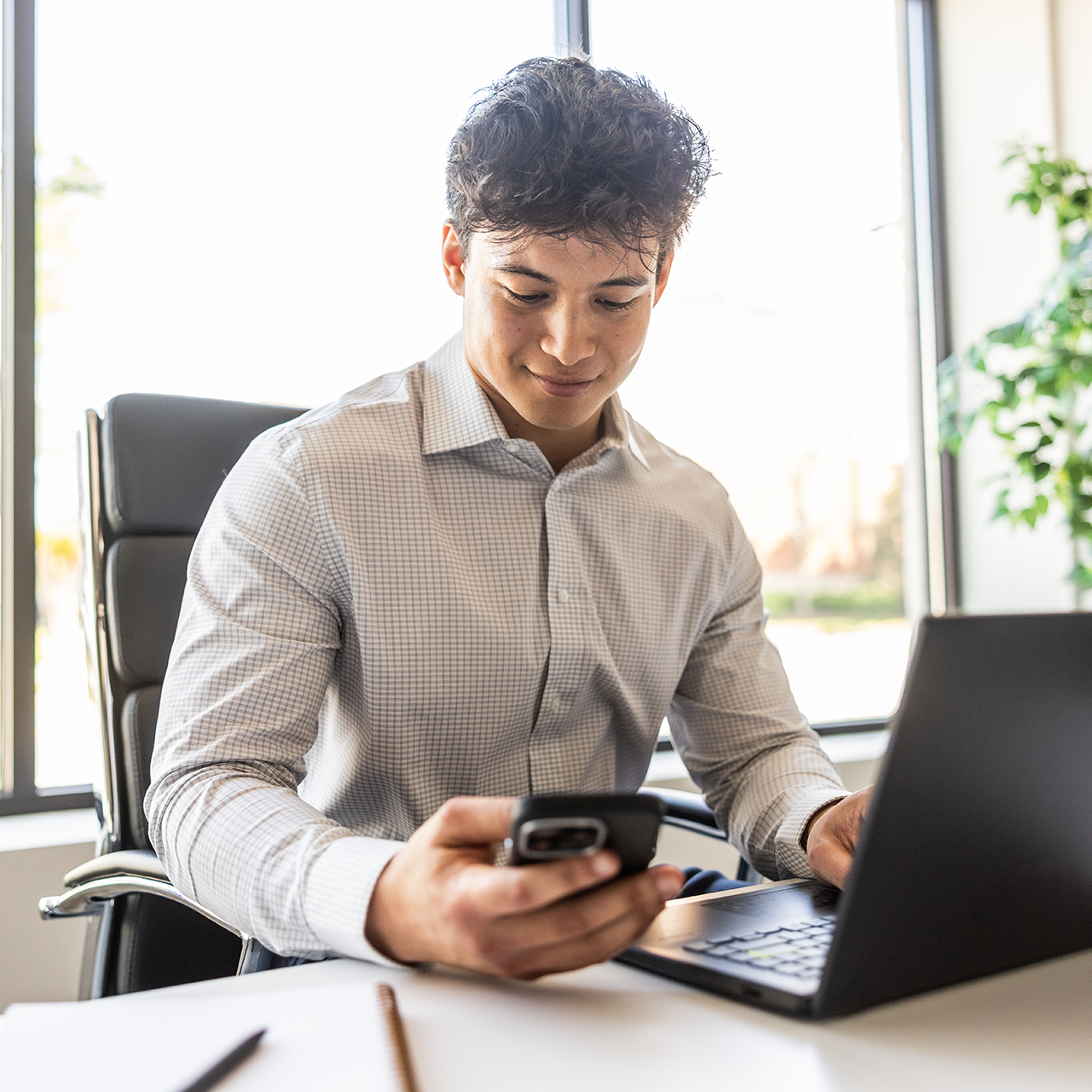 Young businessman using smartphone and laptop in modern conference room