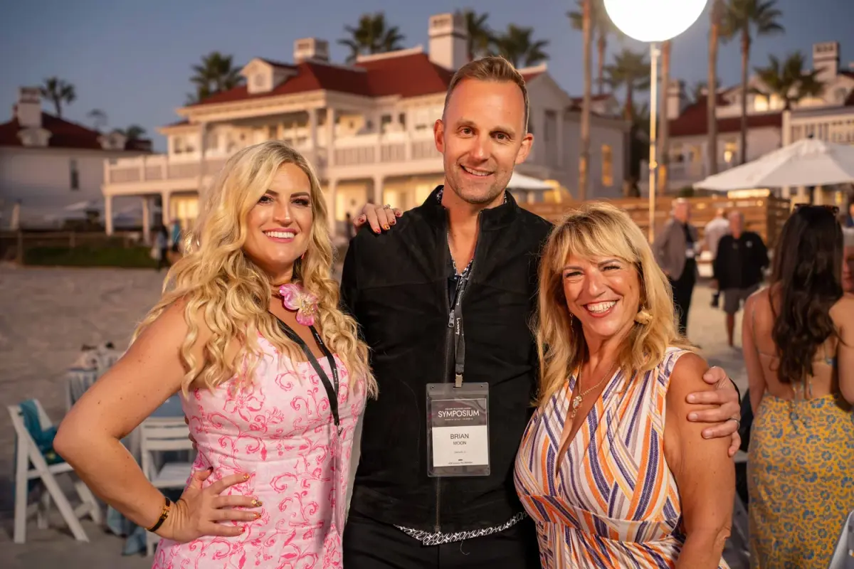 Three guests smiling at the KW Luxury welcome reception on the beach at dusk