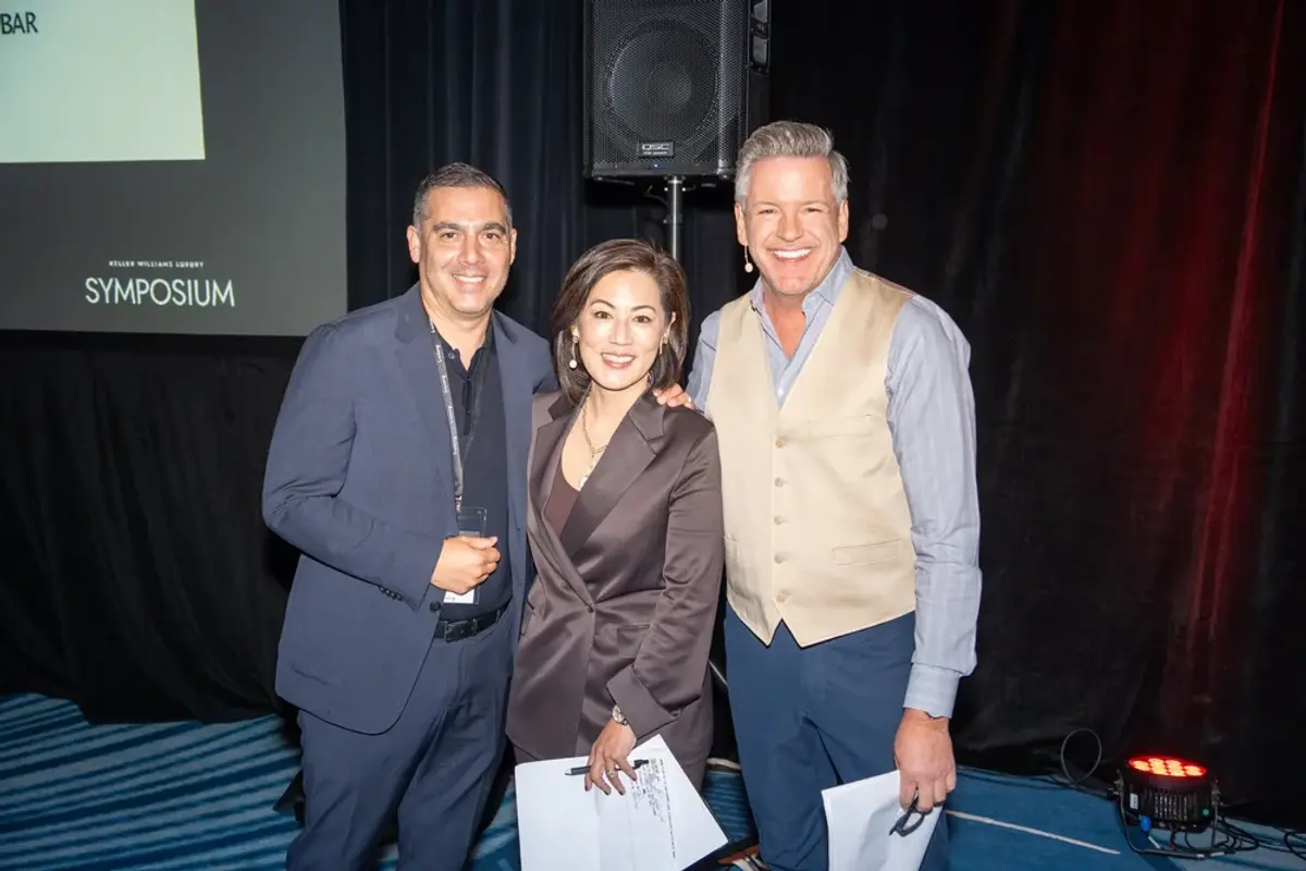 KW Luxury Directors Brady and Caroline smiling near stage with a guest.
