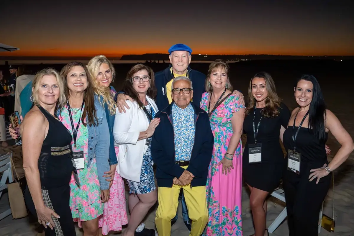 Large group of KW Luxury attendees smiling during a beach reception at sunset.