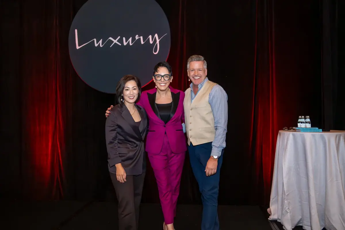 Speaker on stage smiling alongside KW Luxury Directors Brady and Caroline.