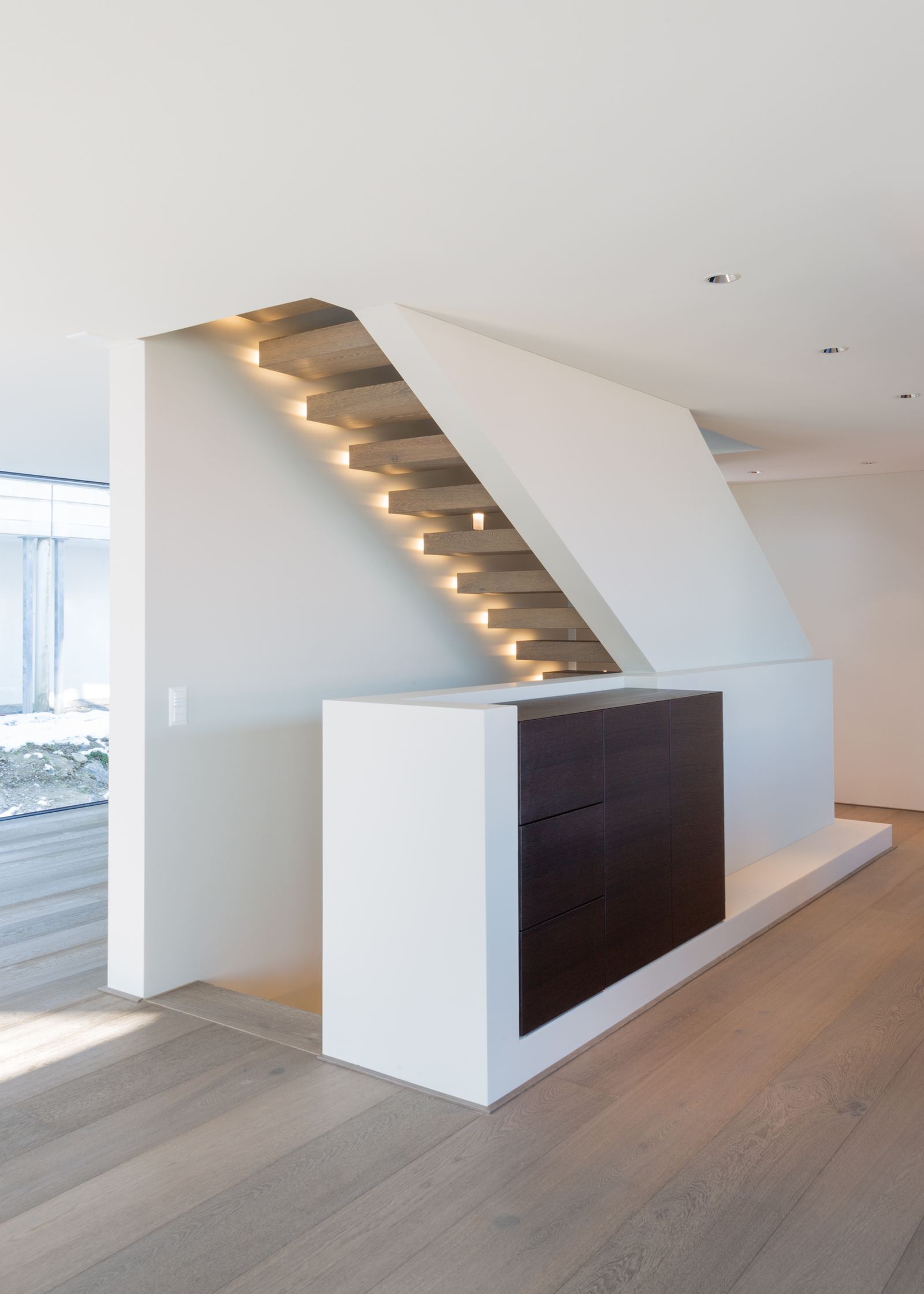 Staircase with step lighting above a dark cabinet
