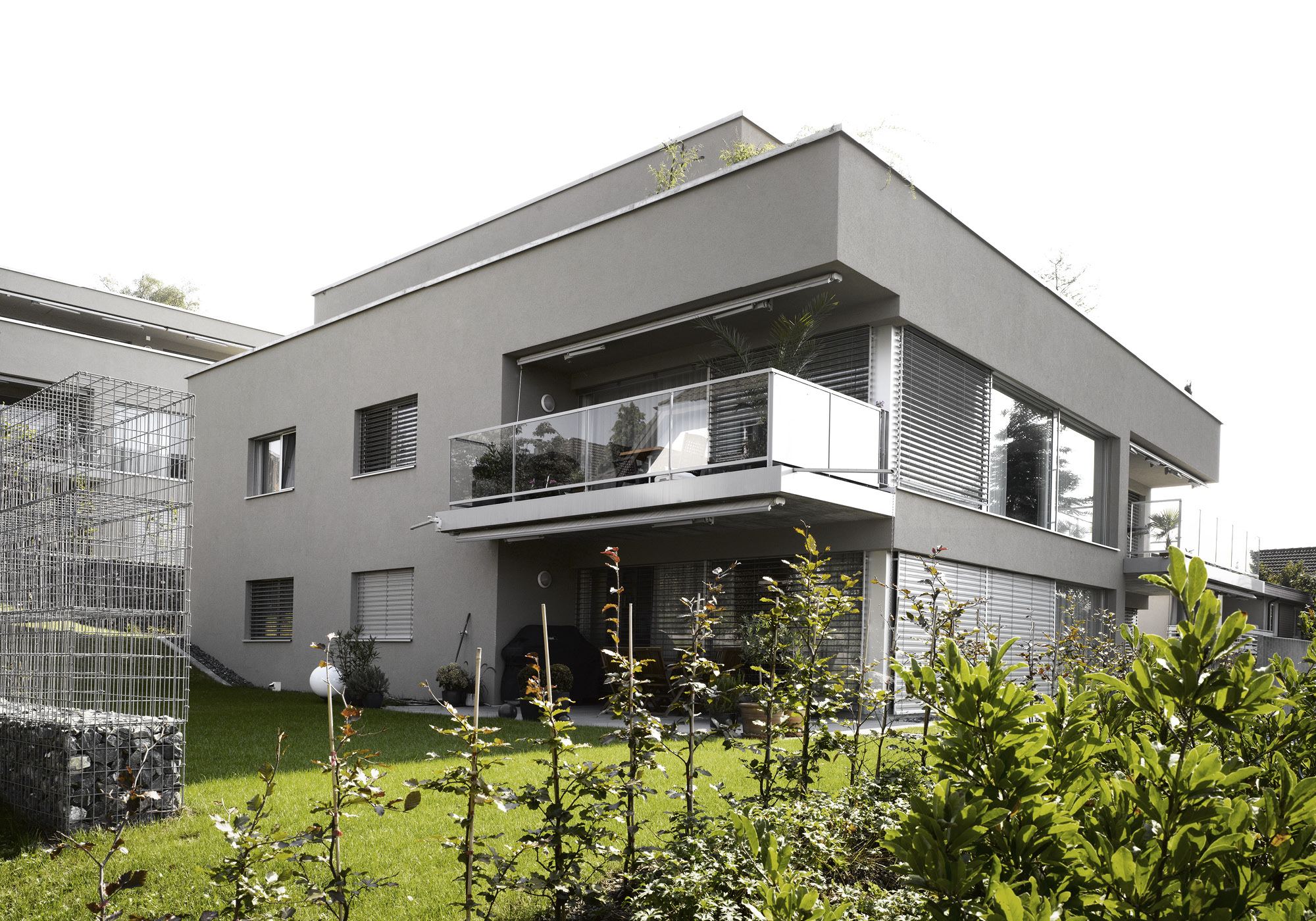 Corner of the house with glass balcony and young trees – Apartment building in Mellingen