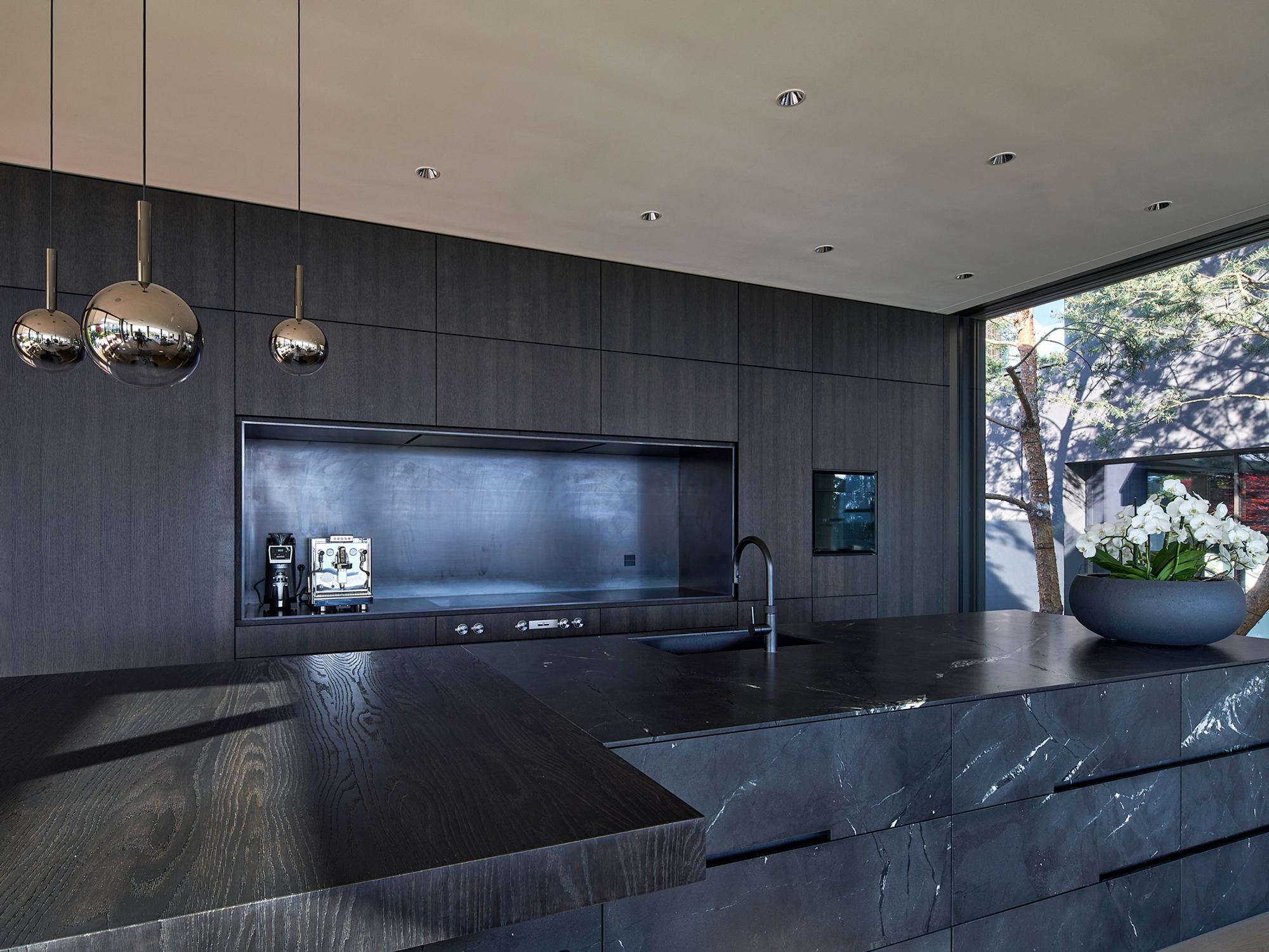 Kitchen island with pendant lights against a dark timber wall – Single-family house in Schindellegi