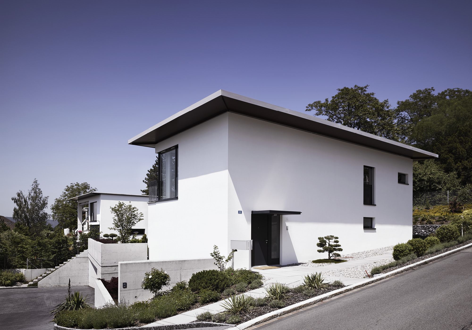 White building with roof overhang on the slope – Single-family house in Uitikon