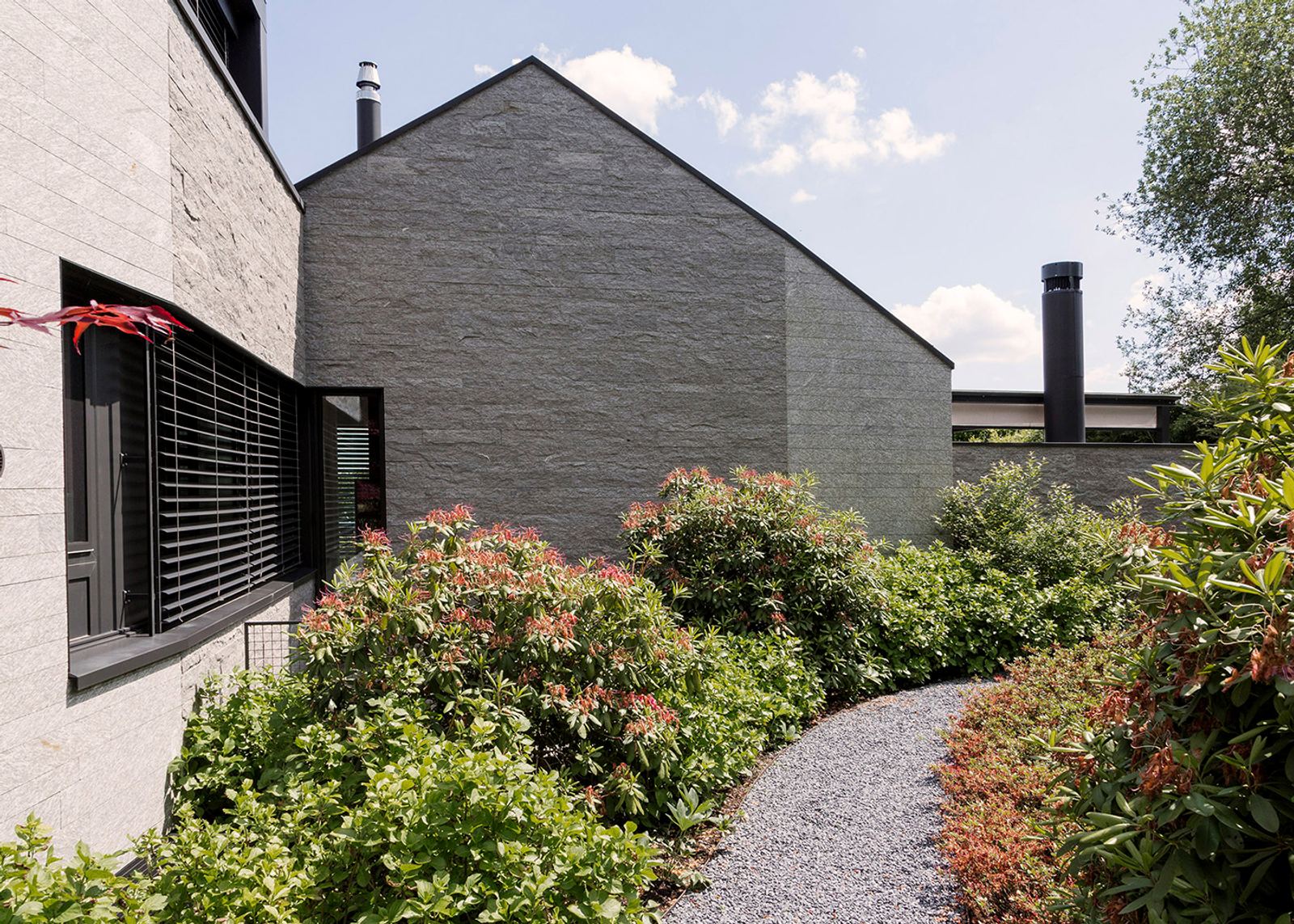 Gravel path between shrubs by the stone house
