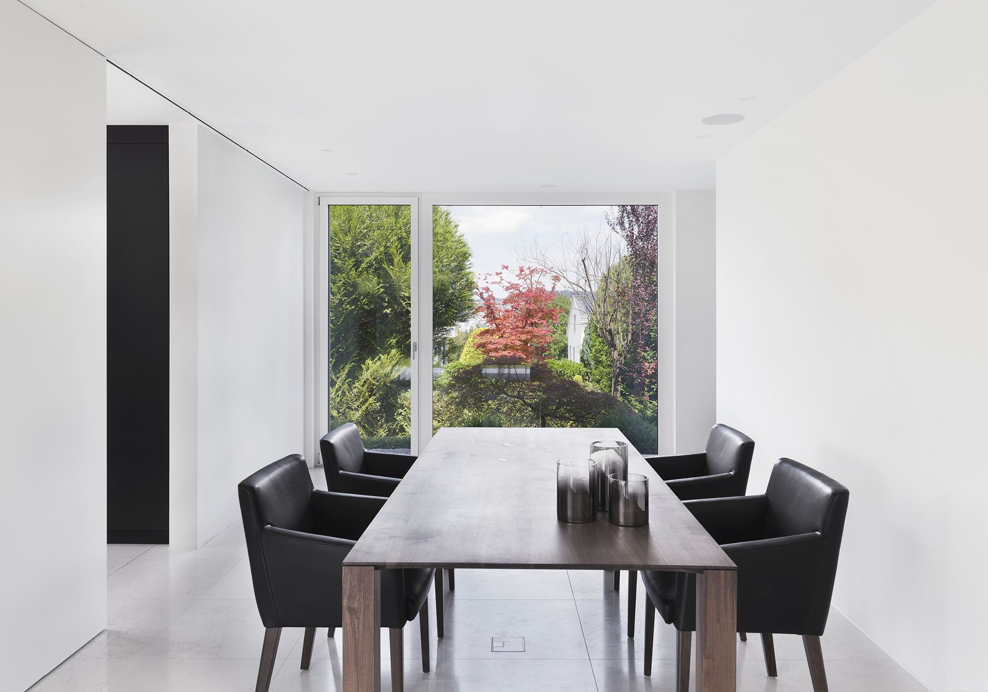 Dining table with black chairs by the glass front – Single-family house in Zürich