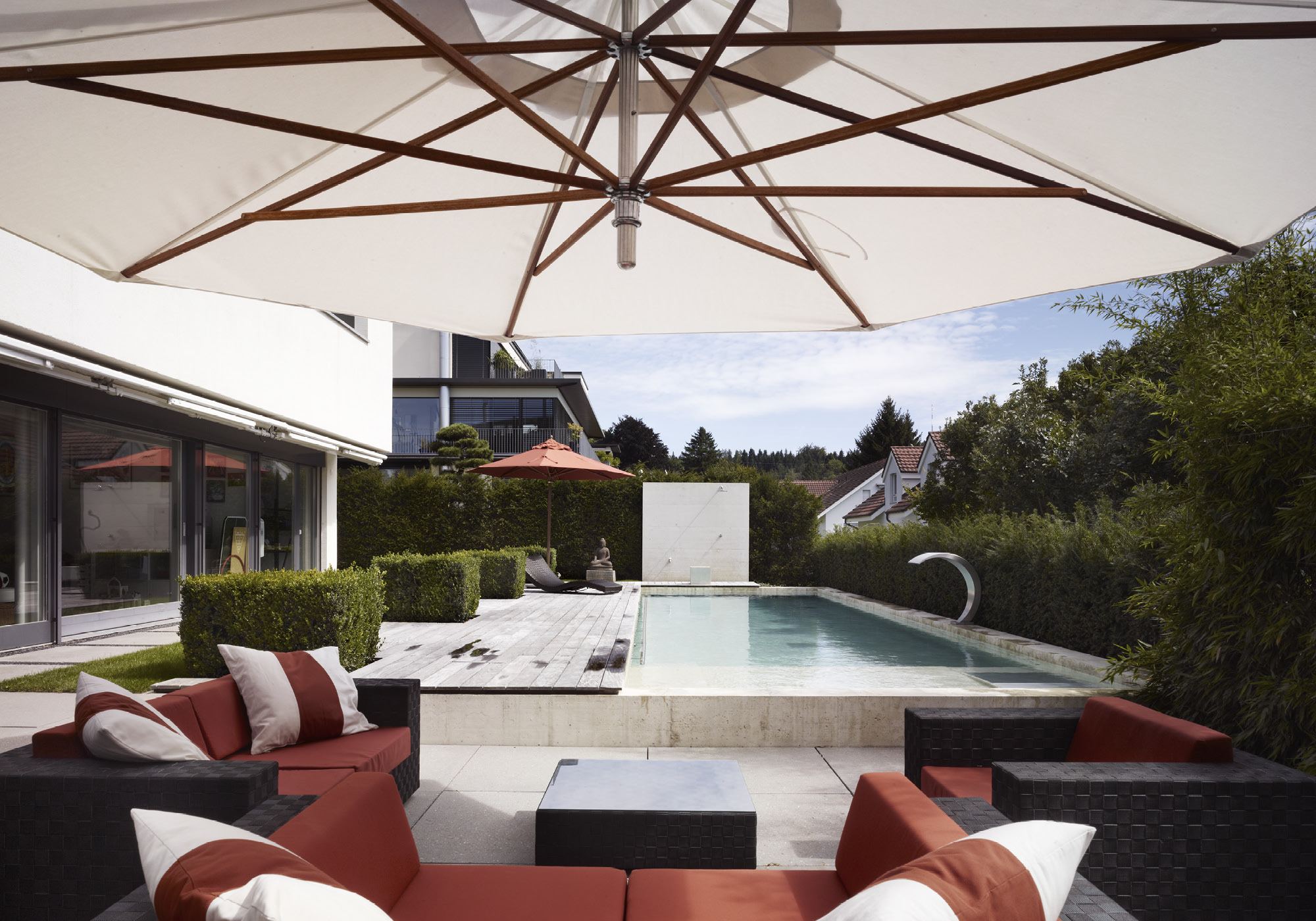 Lounge with red cushions under the parasol – Interiors and landscape, Uitikon