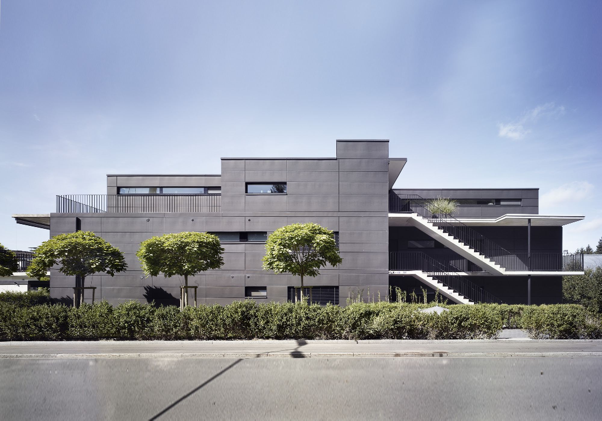 Dark apartment building with globe trees by the street – Apartment building in Uitikon