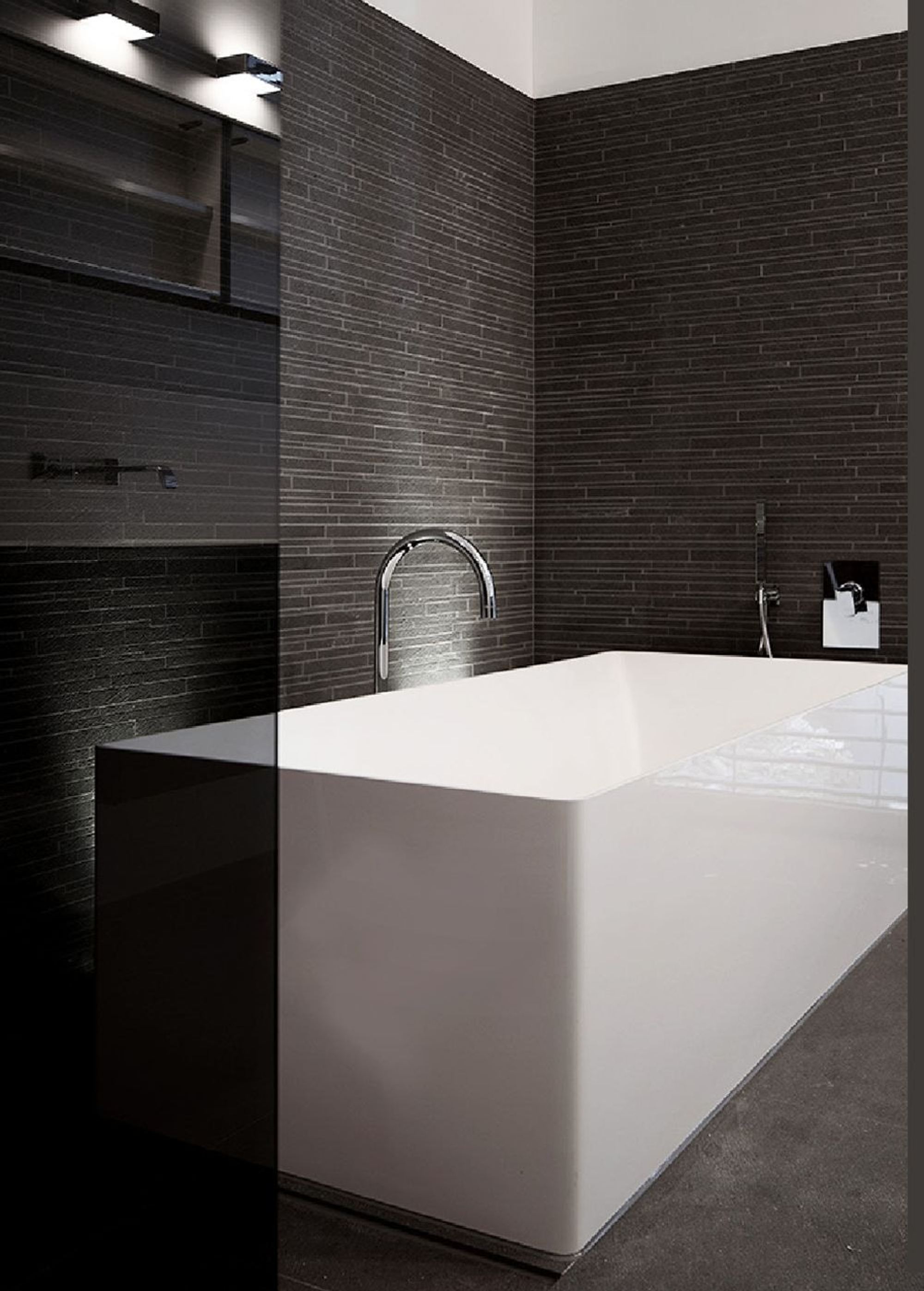 White bathtub against a dark stone wall – Apartment building in Uitikon