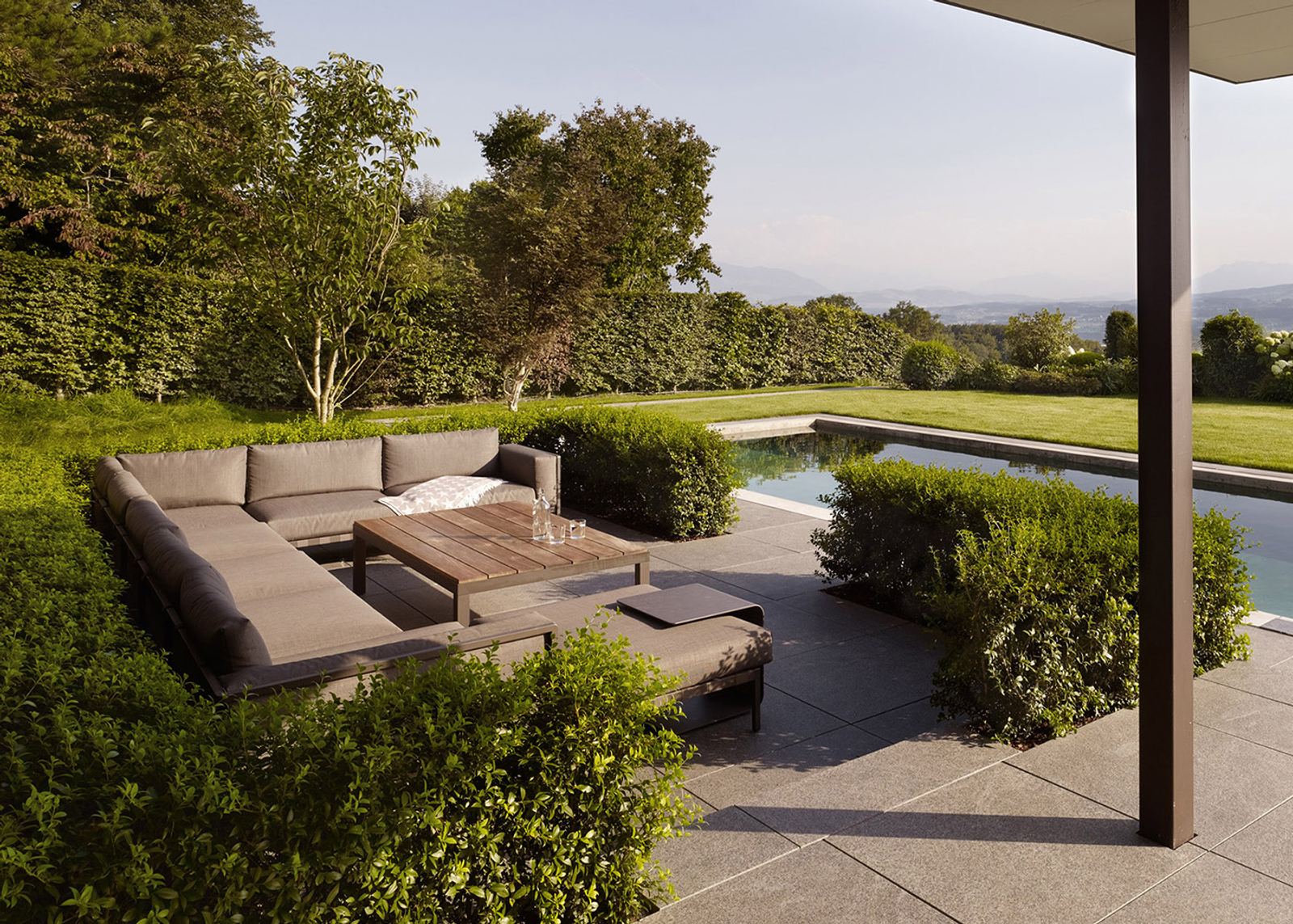 Lounge furniture by the pool between hedges