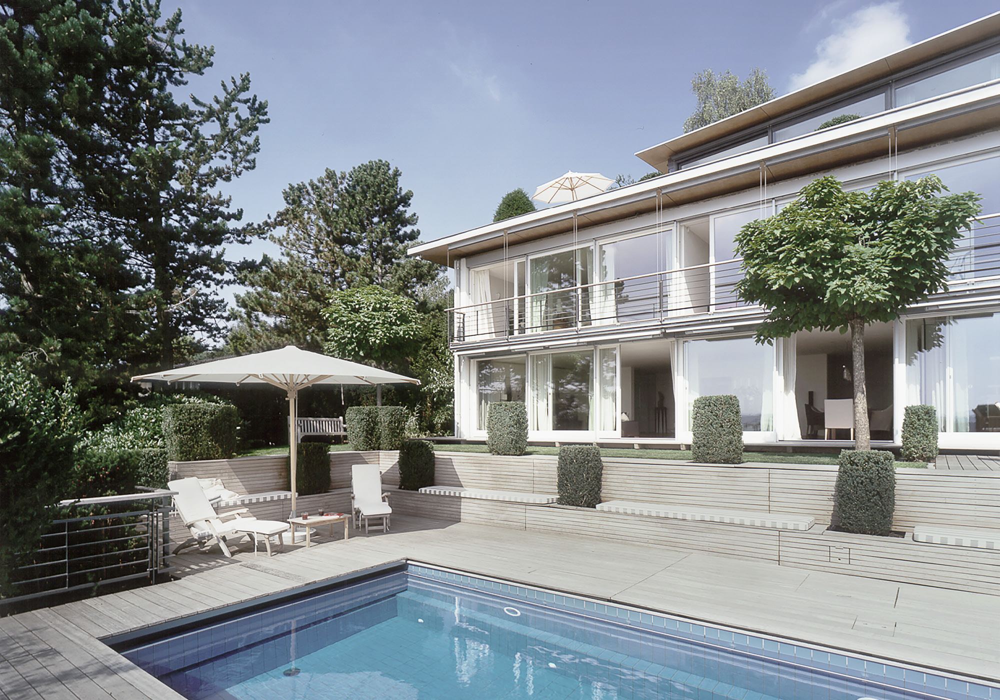 Pool with loungers in front of the light facade – Single-family house