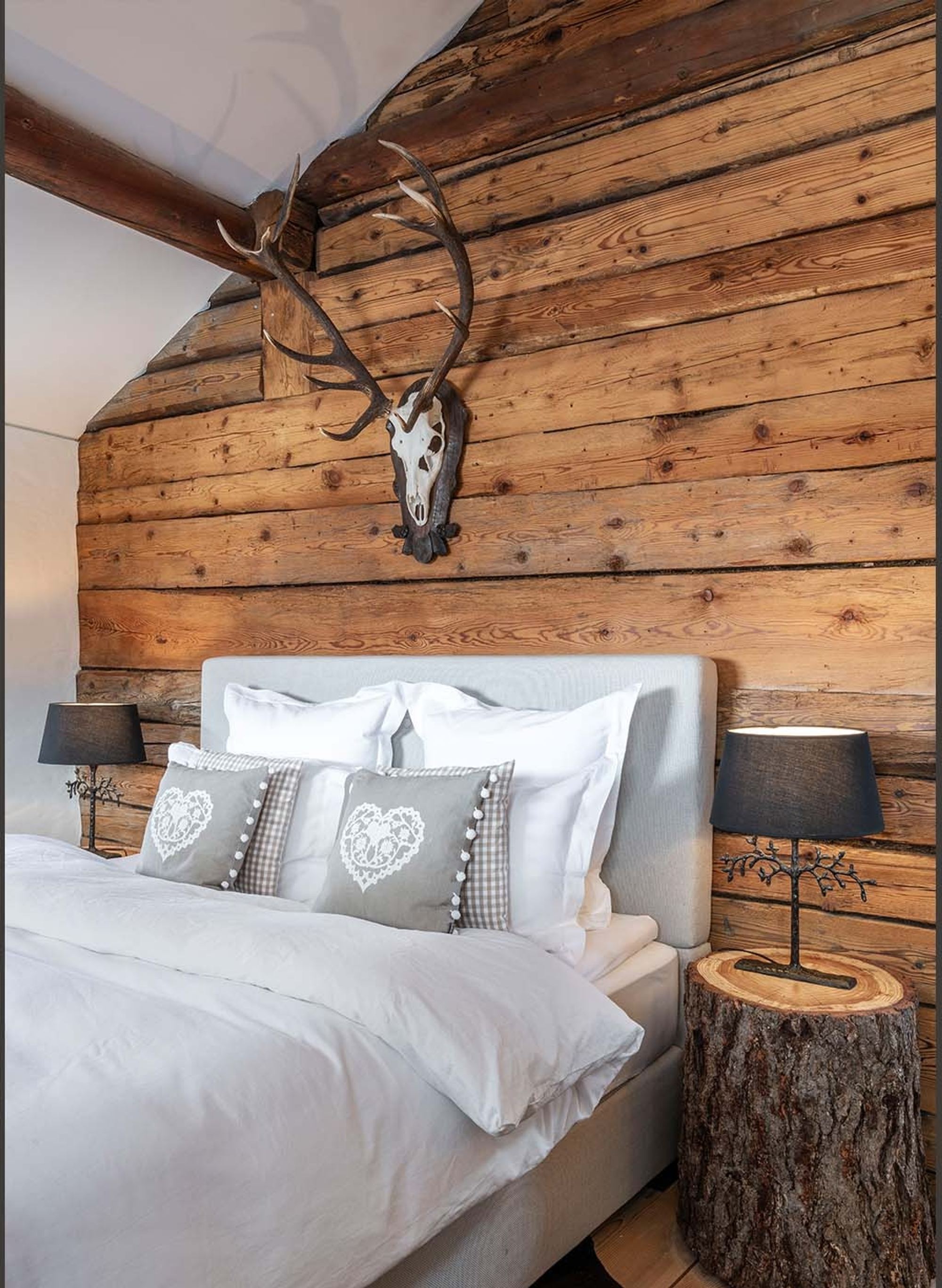 Double bed against reclaimed timber wall with antlers – Historic conversion in Fidaz