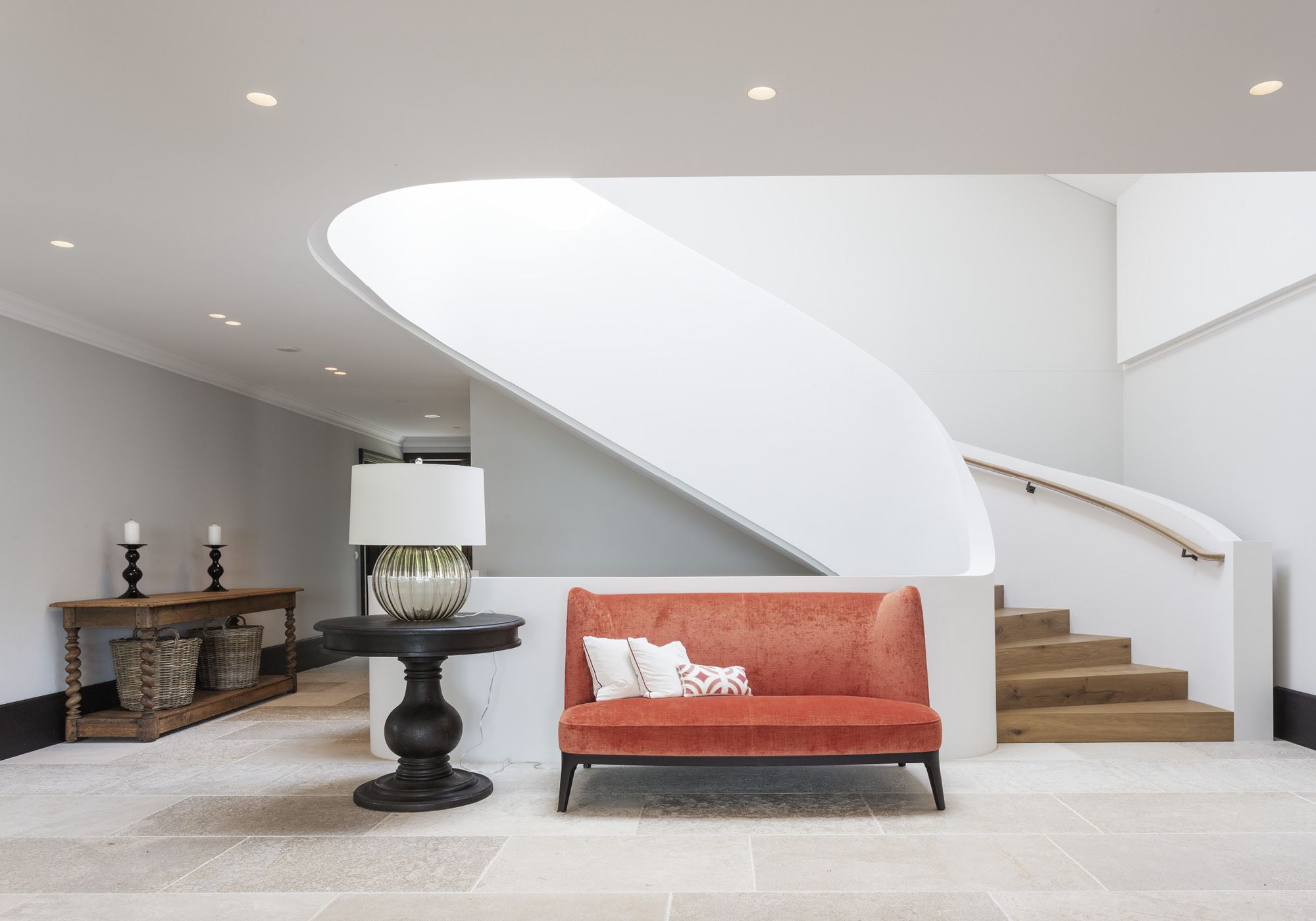 Entrance hall with curved staircase and red sofa – Single-family house in Herrliberg
