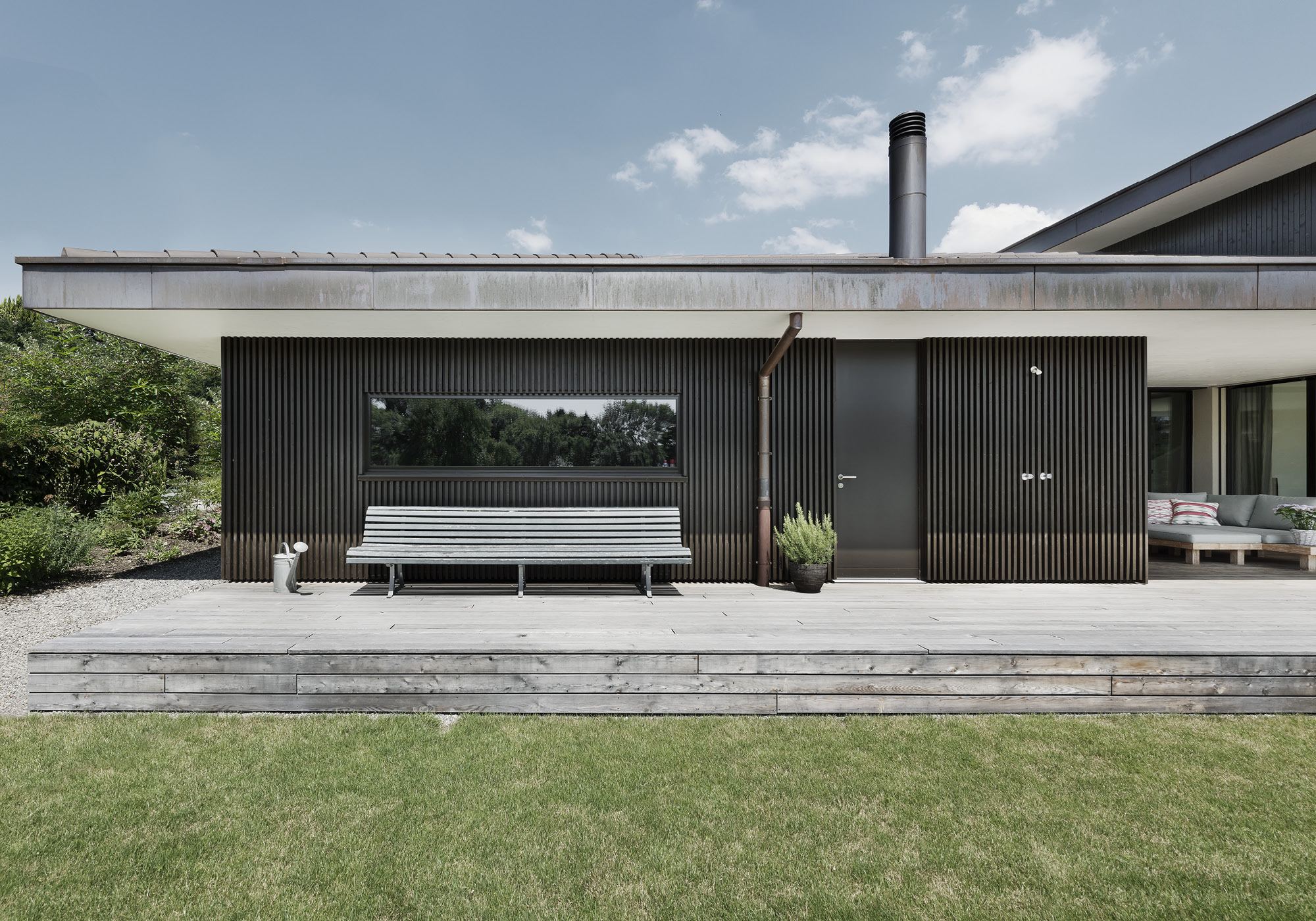 Garden side with dark timber facade and bench – Single-family house in Grüningen