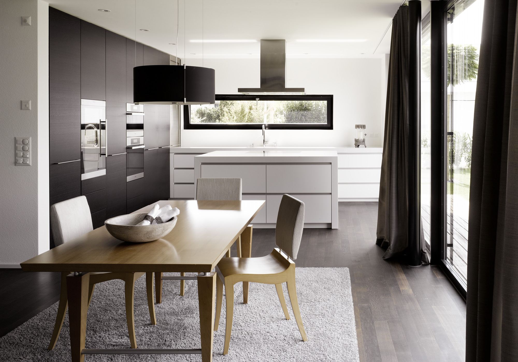 Timber dining table in front of the dark kitchen – Single-family house in Möriken