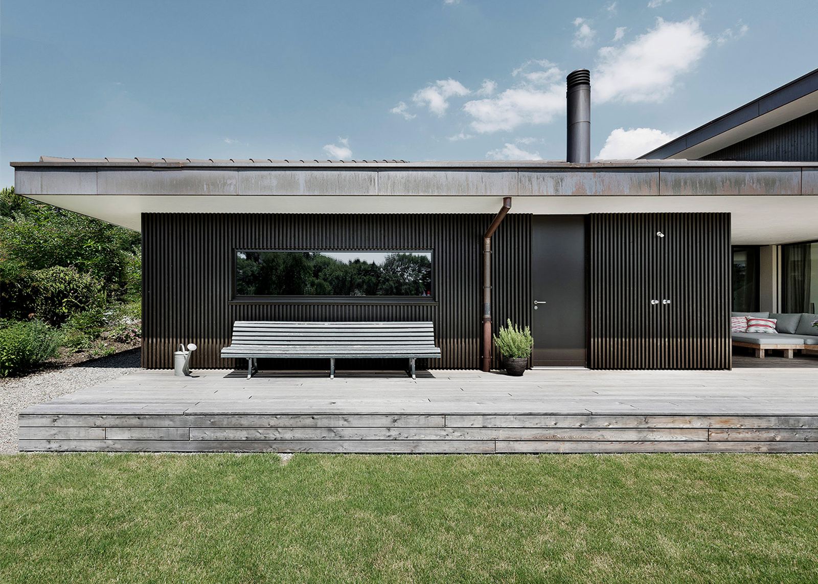 Timber terrace with bench in front of a dark facade