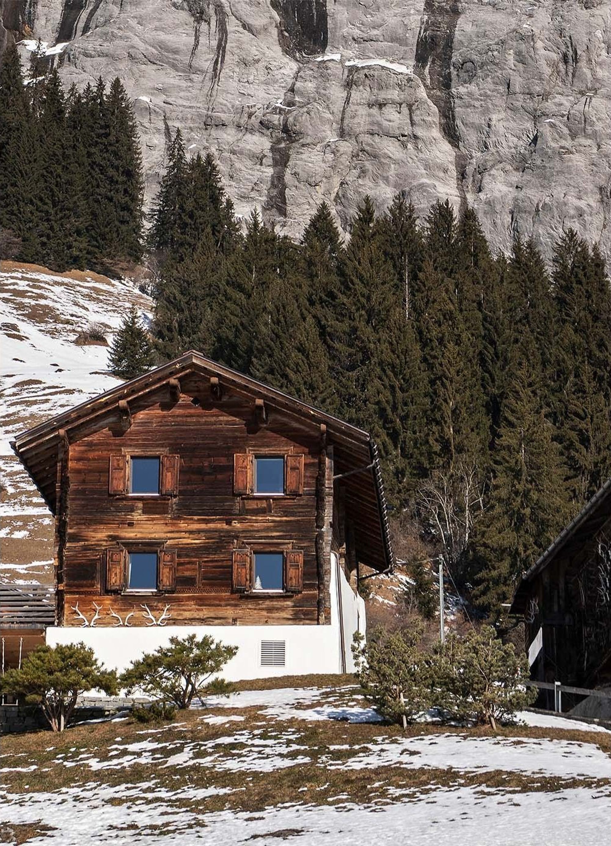 Dark timber log house in front of a rock face and forest – Historic conversion in Fidaz