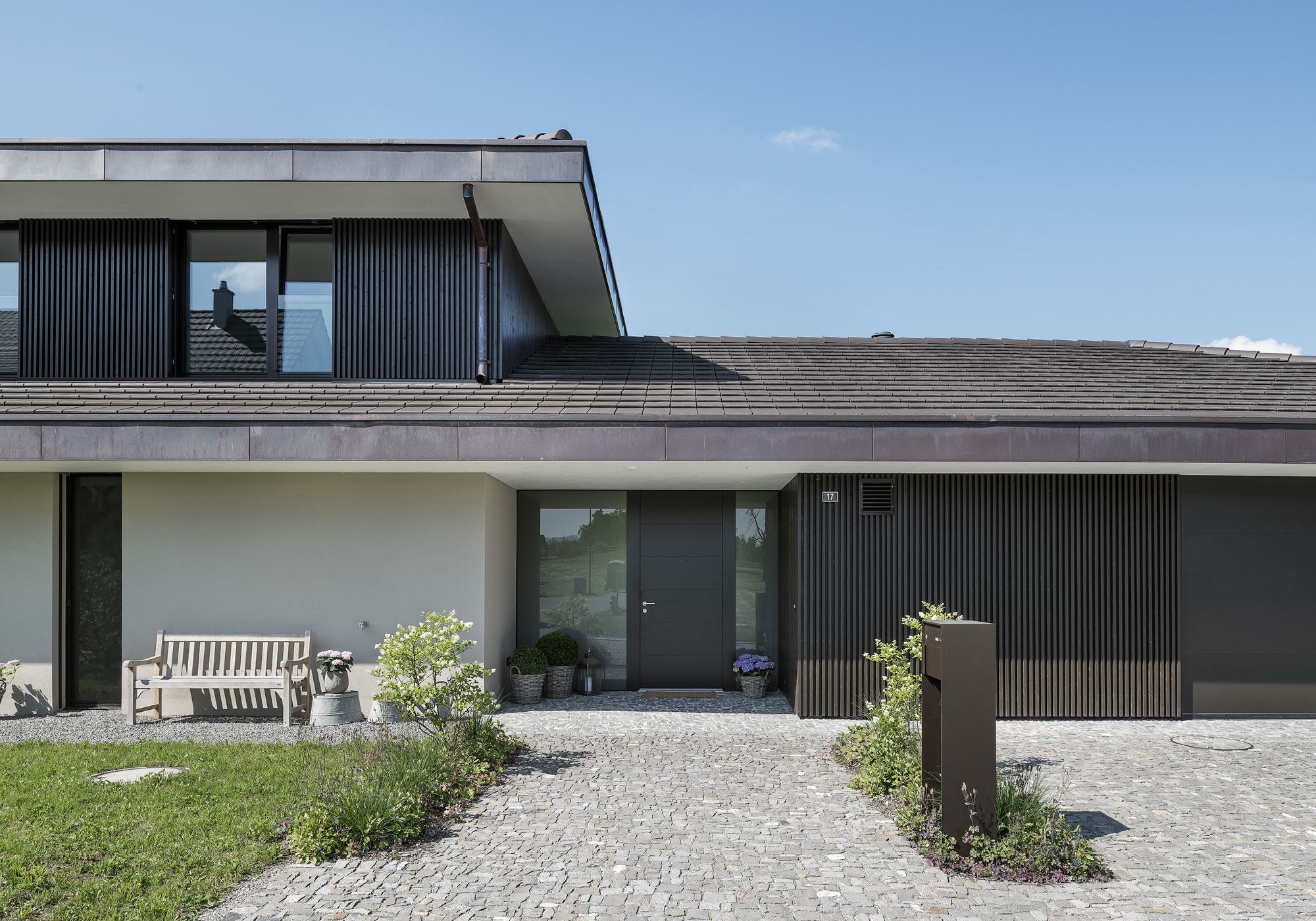 Entrance with dark timber facade and gravel path – Single-family house in Grüningen