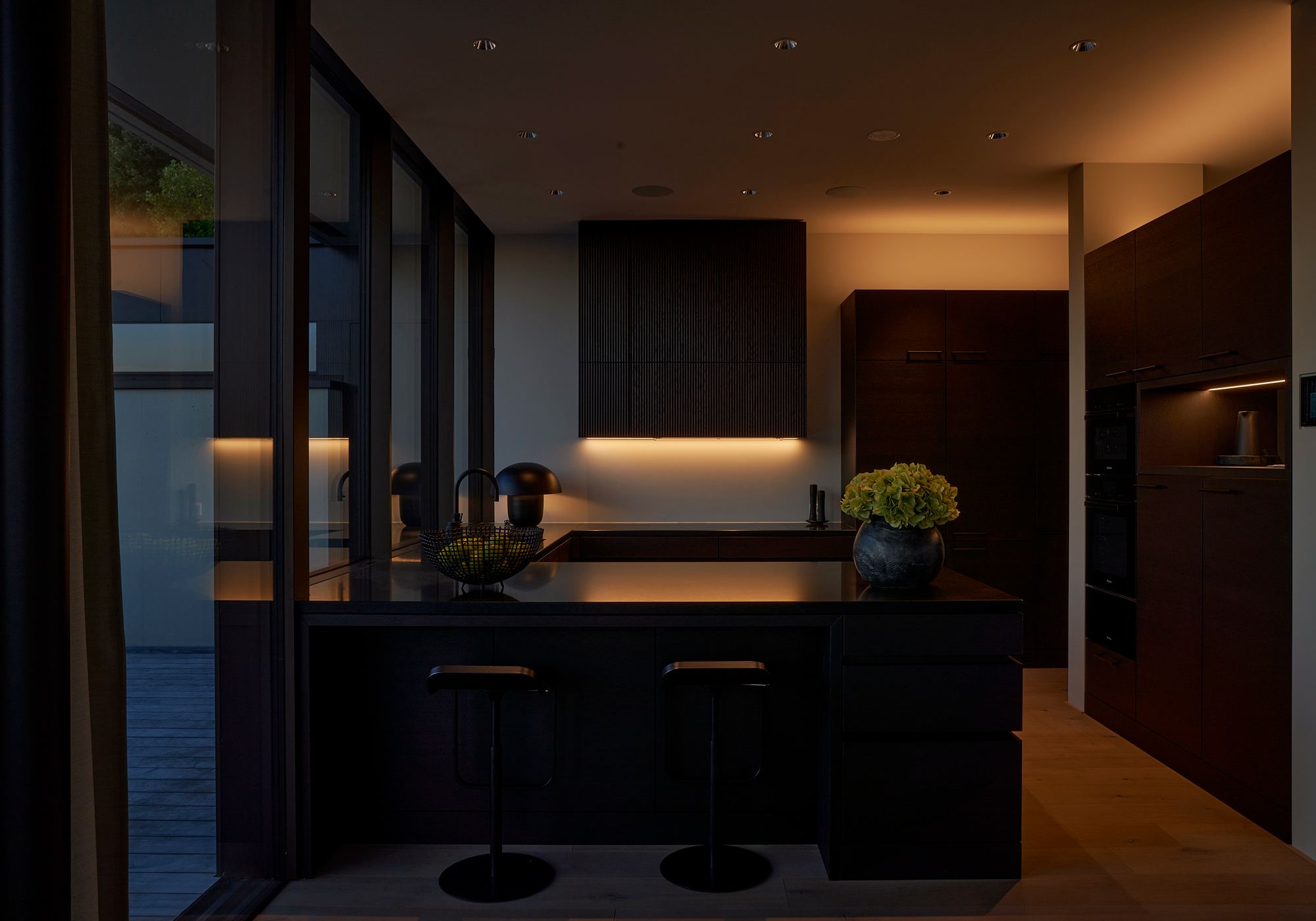 Kitchen with dark fronts and bar stools in the evening – Single-family house in Uitikon